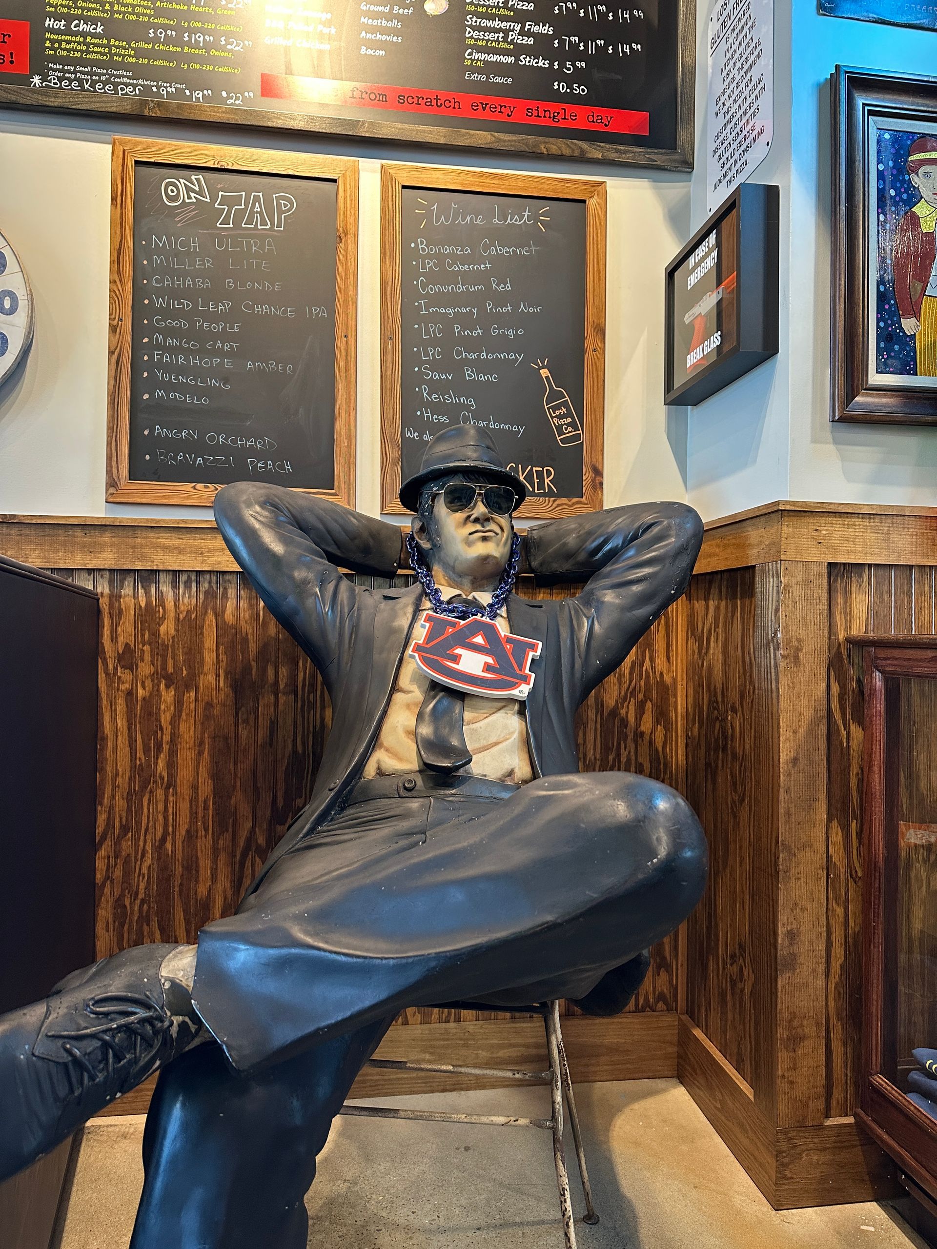 Statue of a man in a suit, relaxing with arms behind his head, inside a restaurant with wooden paneling.