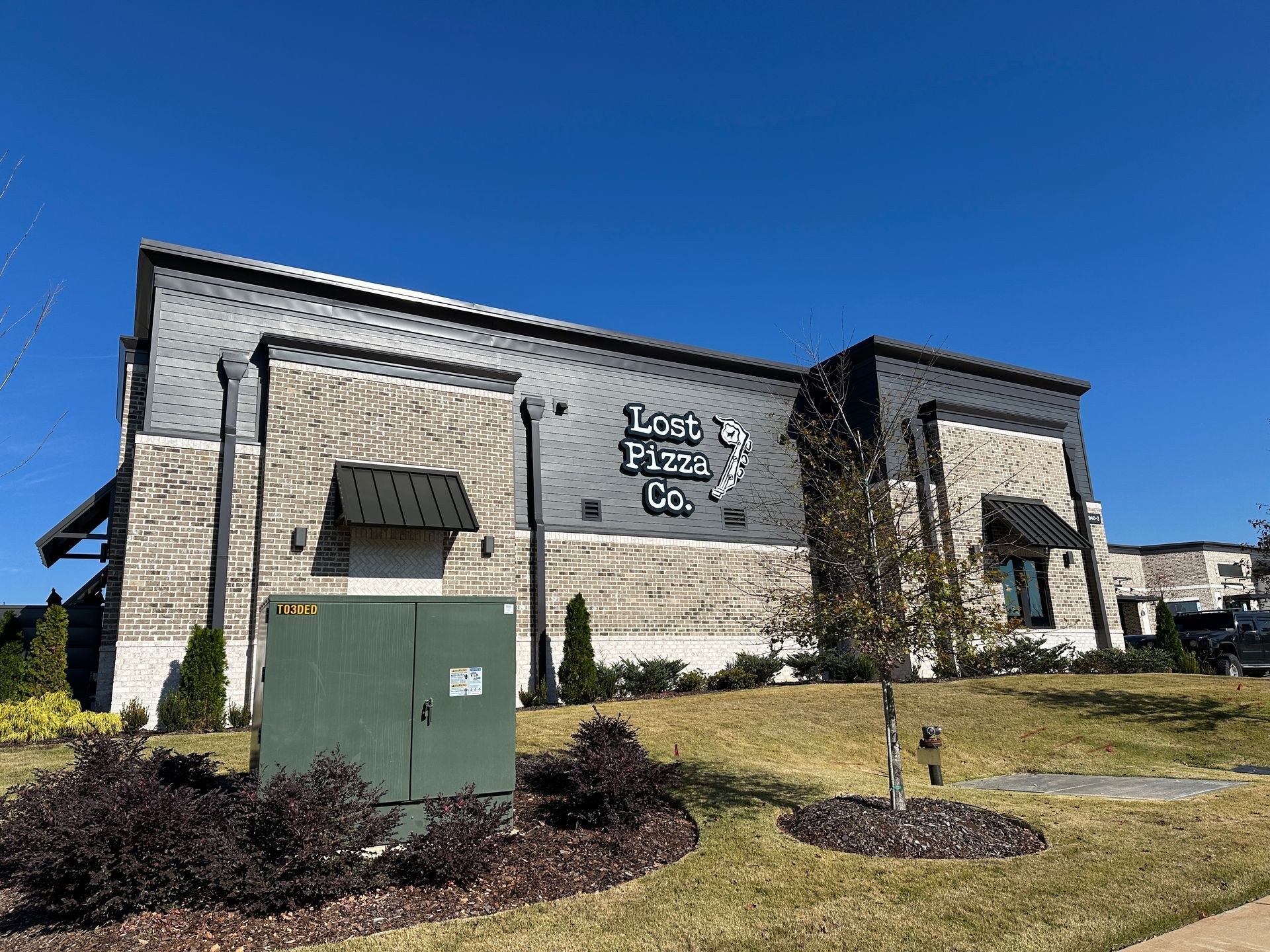 Exterior of 1245 Theatre Co. building under a blue sky. Gray and brick facade, dark awnings, green utility box.