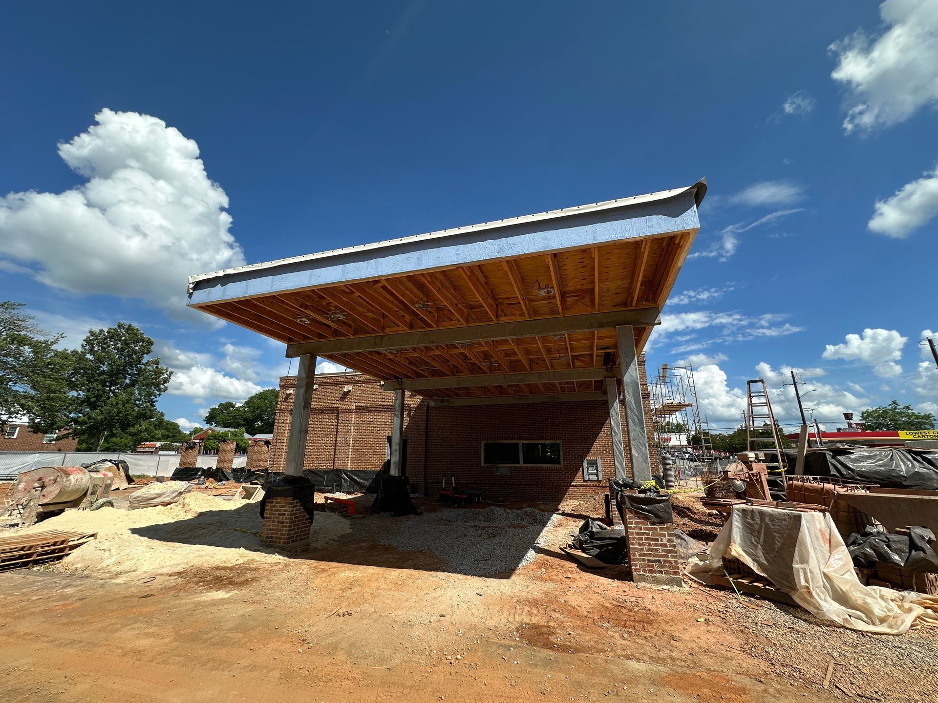 Large bank drive-thru structure under construction on a dirt lot with brick walls and a blue sky.