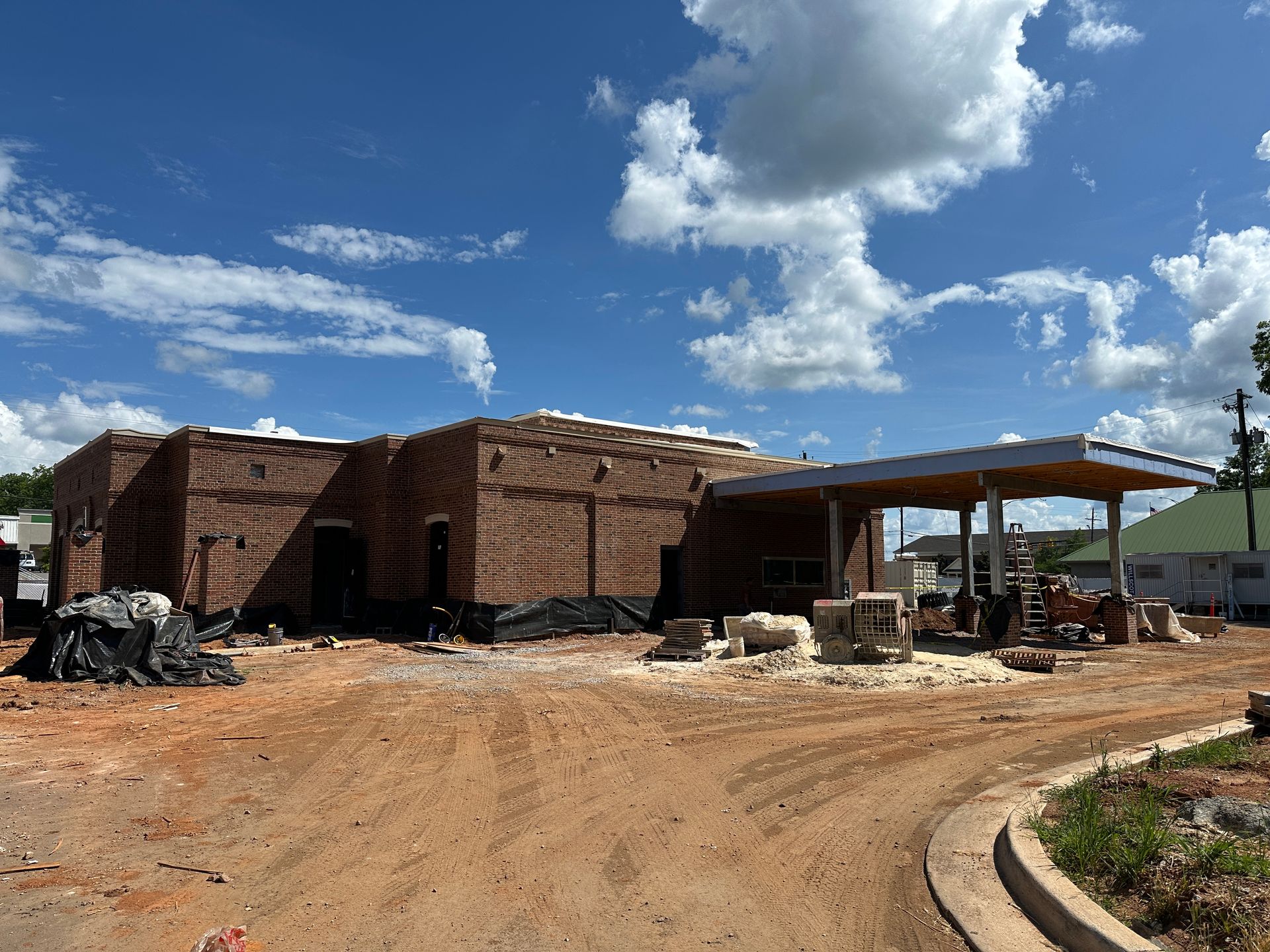 Partly built bank structure on a dirt lot under a blue sky with clouds, construction materials nearby