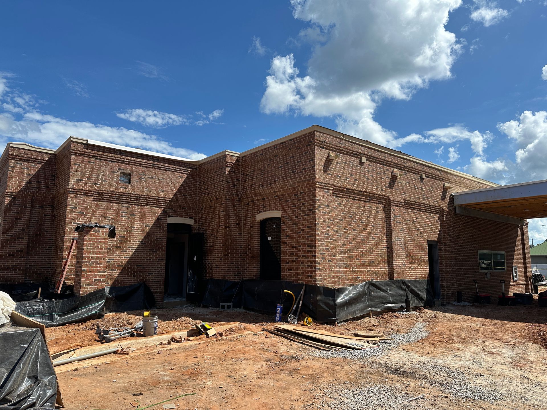 Partially built brick bank with black construction wrap under a blue sky with clouds