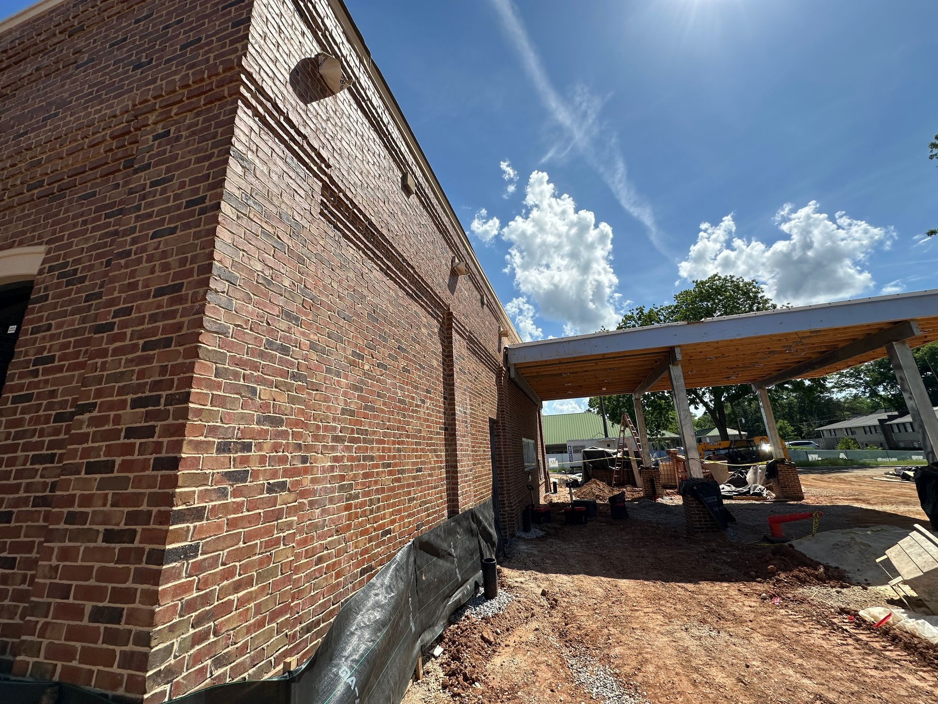 Brick building exterior with covered patio under construction on a sunny day