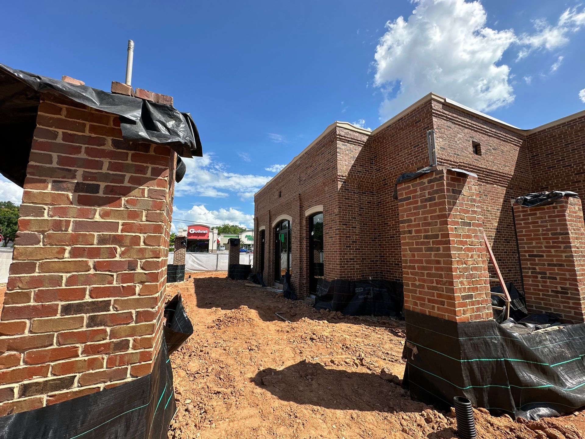 Brick bank under construction with brick walls, black tarps, and clear blue sky