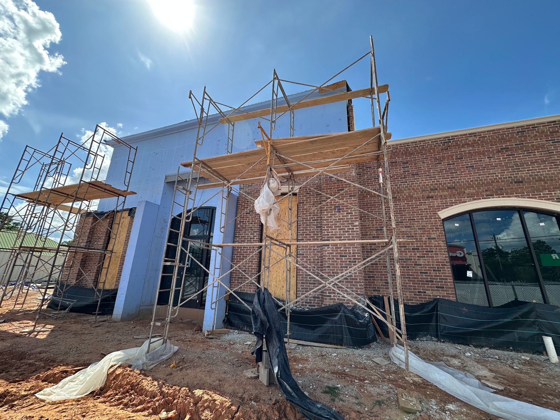 Construction site with scaffolding around a partially finished brick building under a bright blue sky