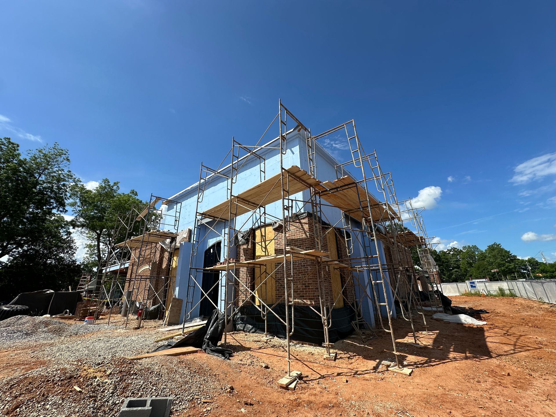 Bank under construction with blue tarp, wooden scaffolding, and metal roof frame under a clear blue sky