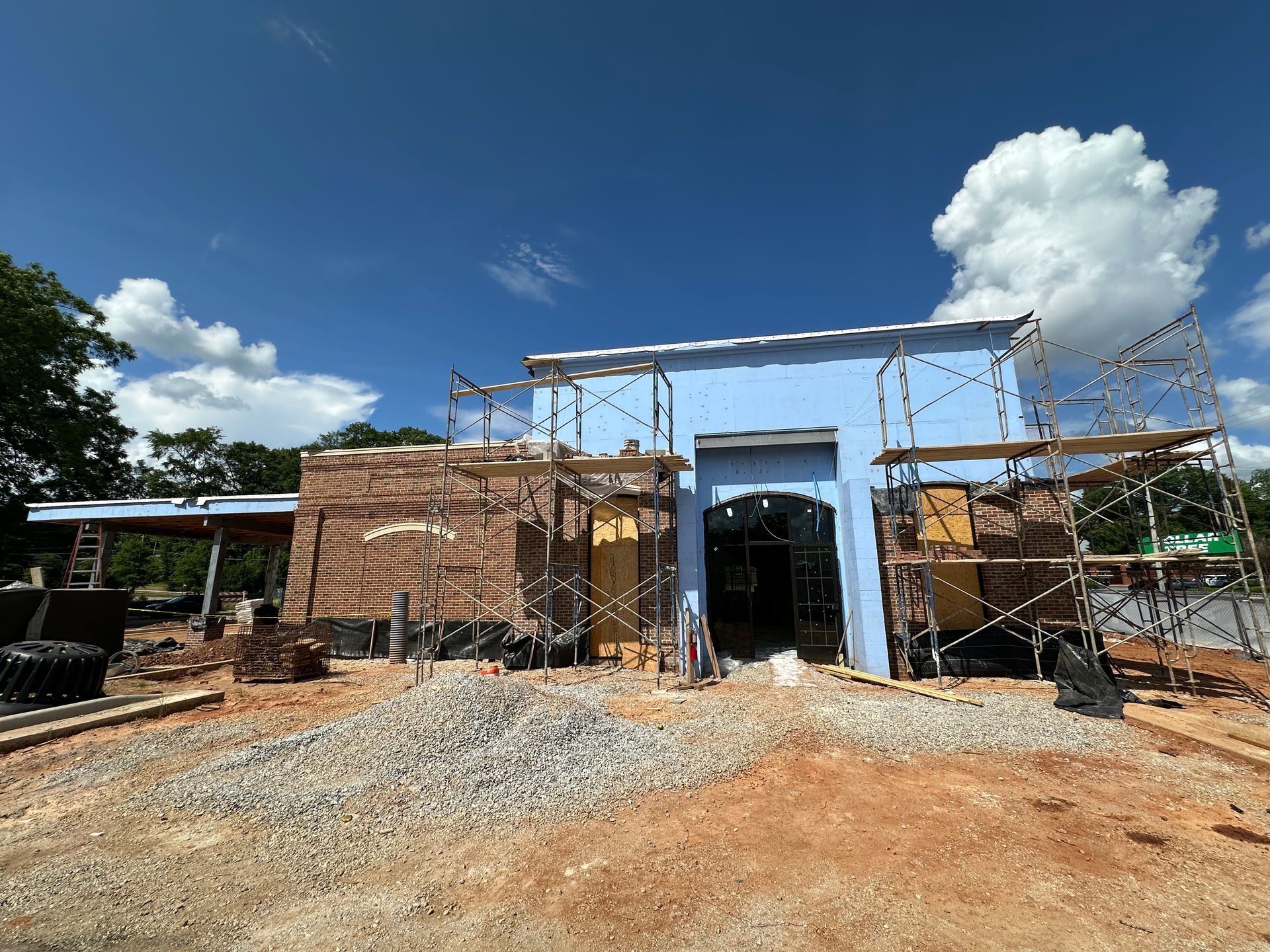 Partially built brick structure with scaffolding and a large metal frame under a bright blue sky