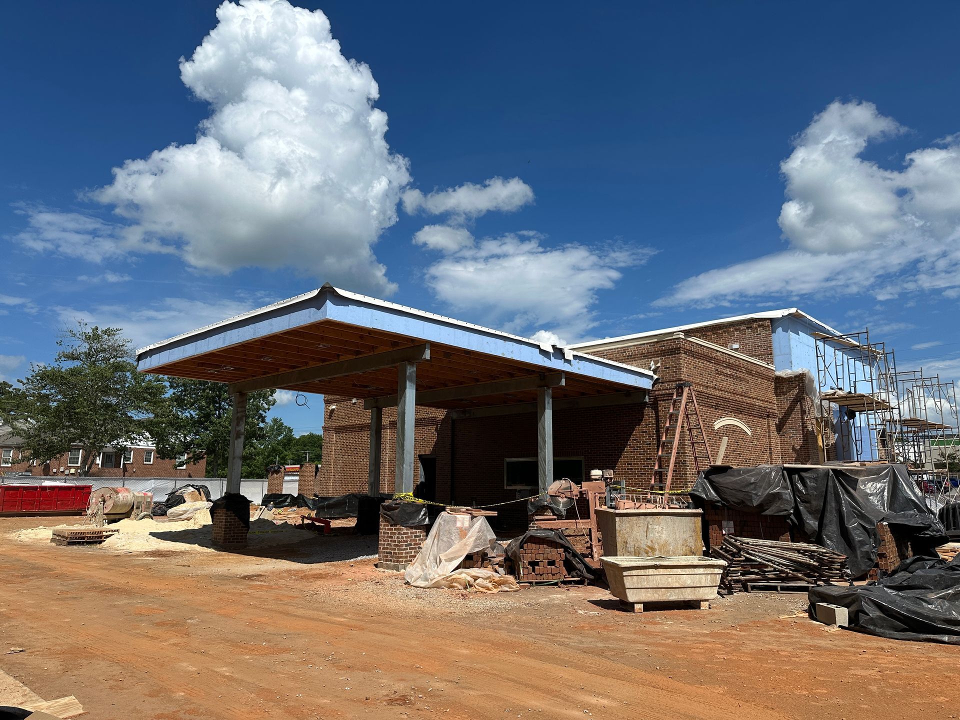 Partially built brick bank with a metal roof under a bright blue sky and clouds