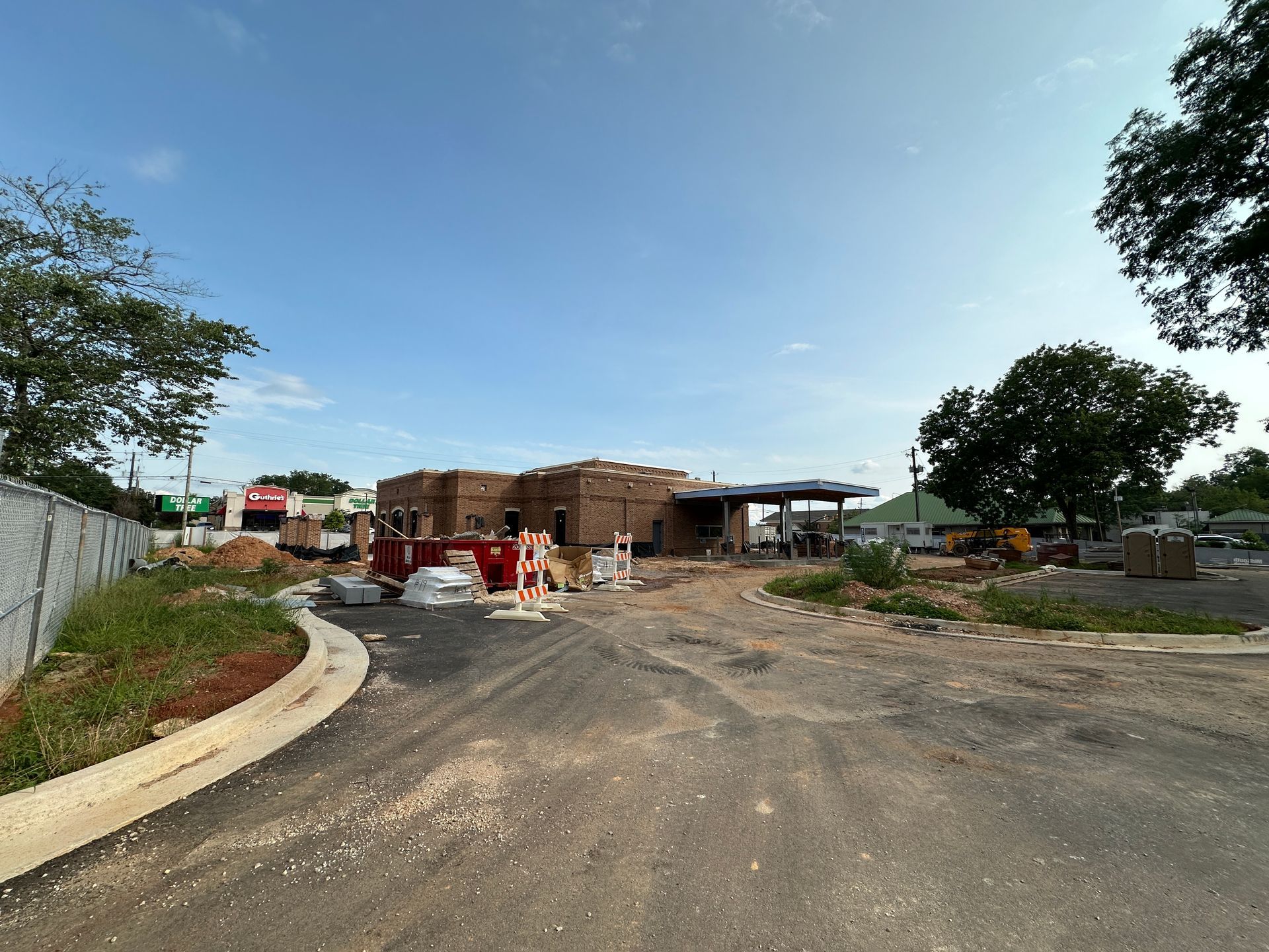 Construction site with roadwork barriers, dirt road, and buildings under a blue sky