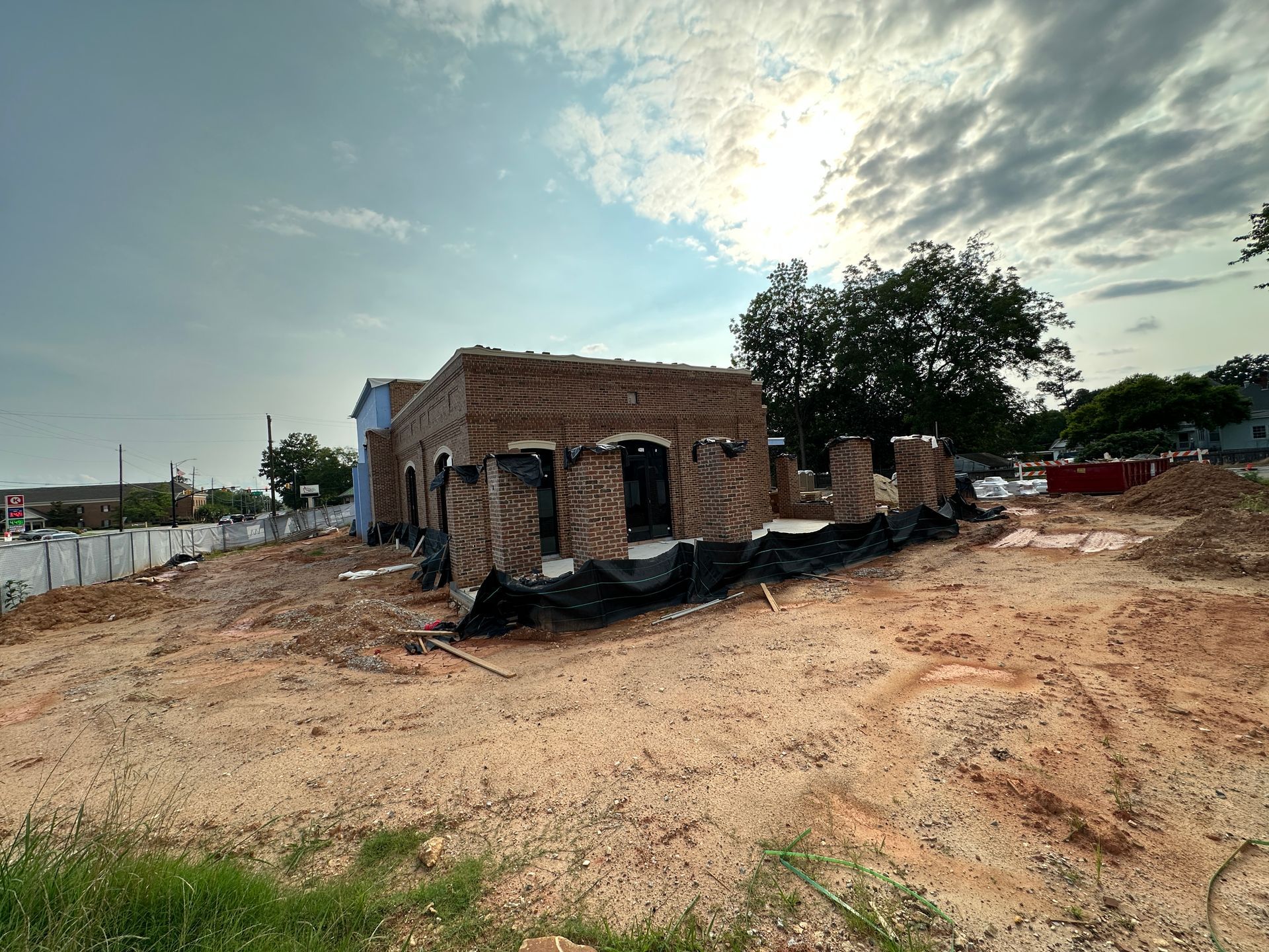 Partially built brick house on a sandy lot under a cloudy sky