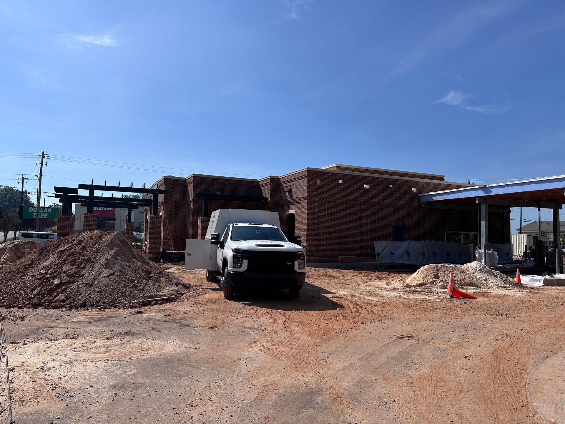 White pickup truck at a construction site with piles of dirt and a partially built brick structure under a blue sky