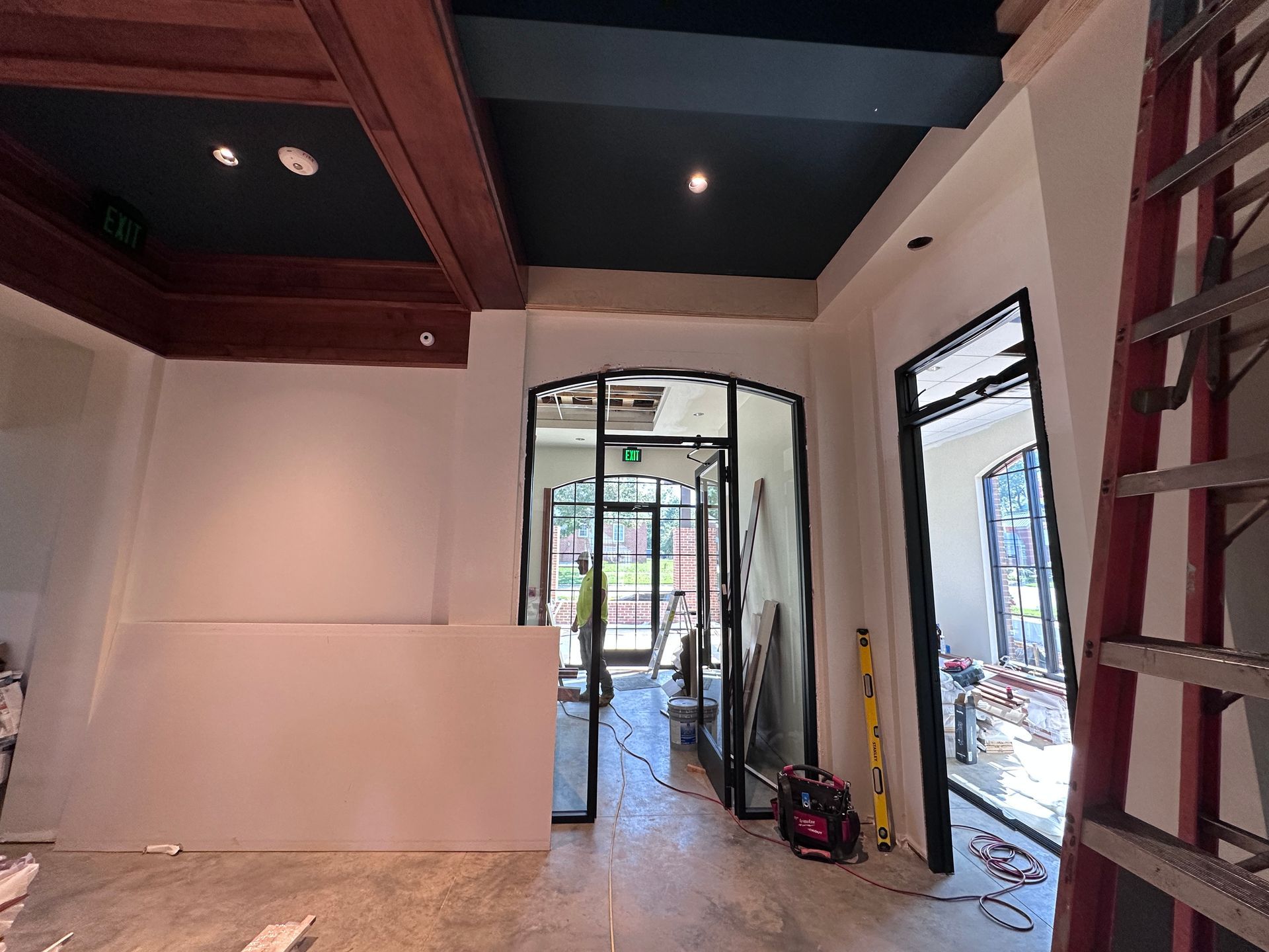 Unfinished interior room with white walls, dark ceiling beams, and construction tools near an open doorway.