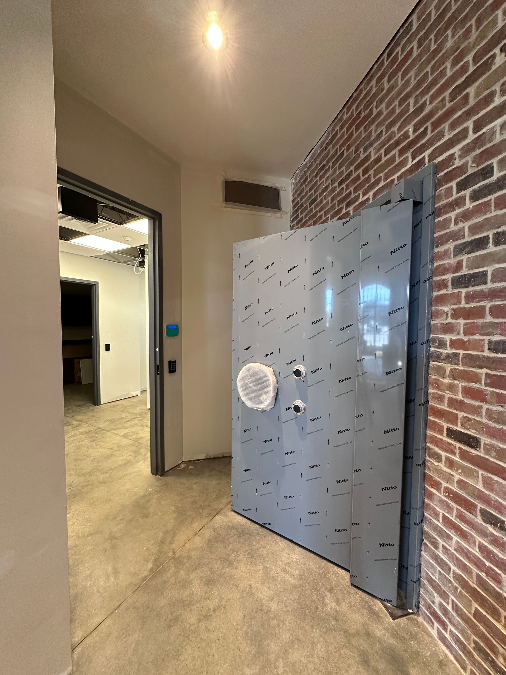 Open vault door in a brick-walled hallway, with a lit room visible beyond.