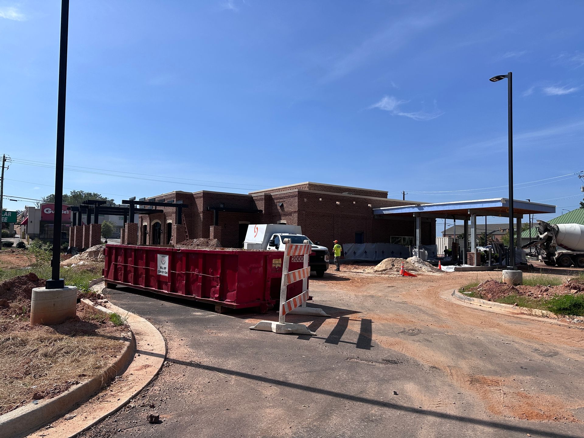 Red dumpster at a construction site beside a small brick building under a blue sky.
