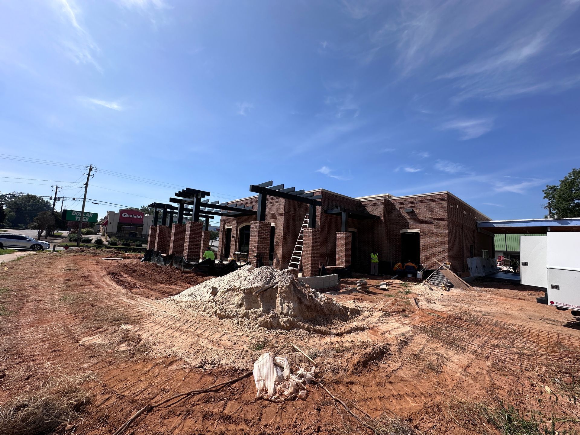 Brick houses under construction along a dirt road, with piles of rubble and a blue sky.