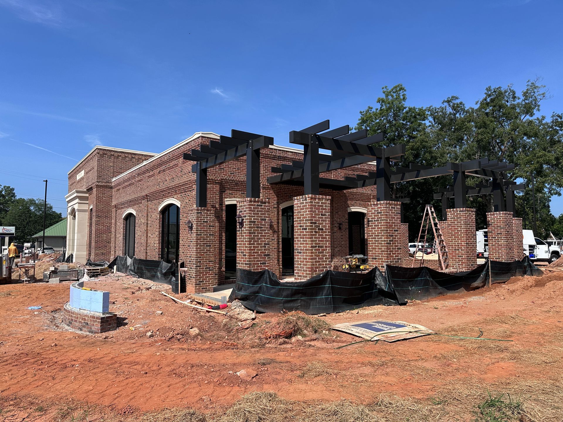 Partially built red-brick house with wooden roof framing on a dirt lot under a blue sky