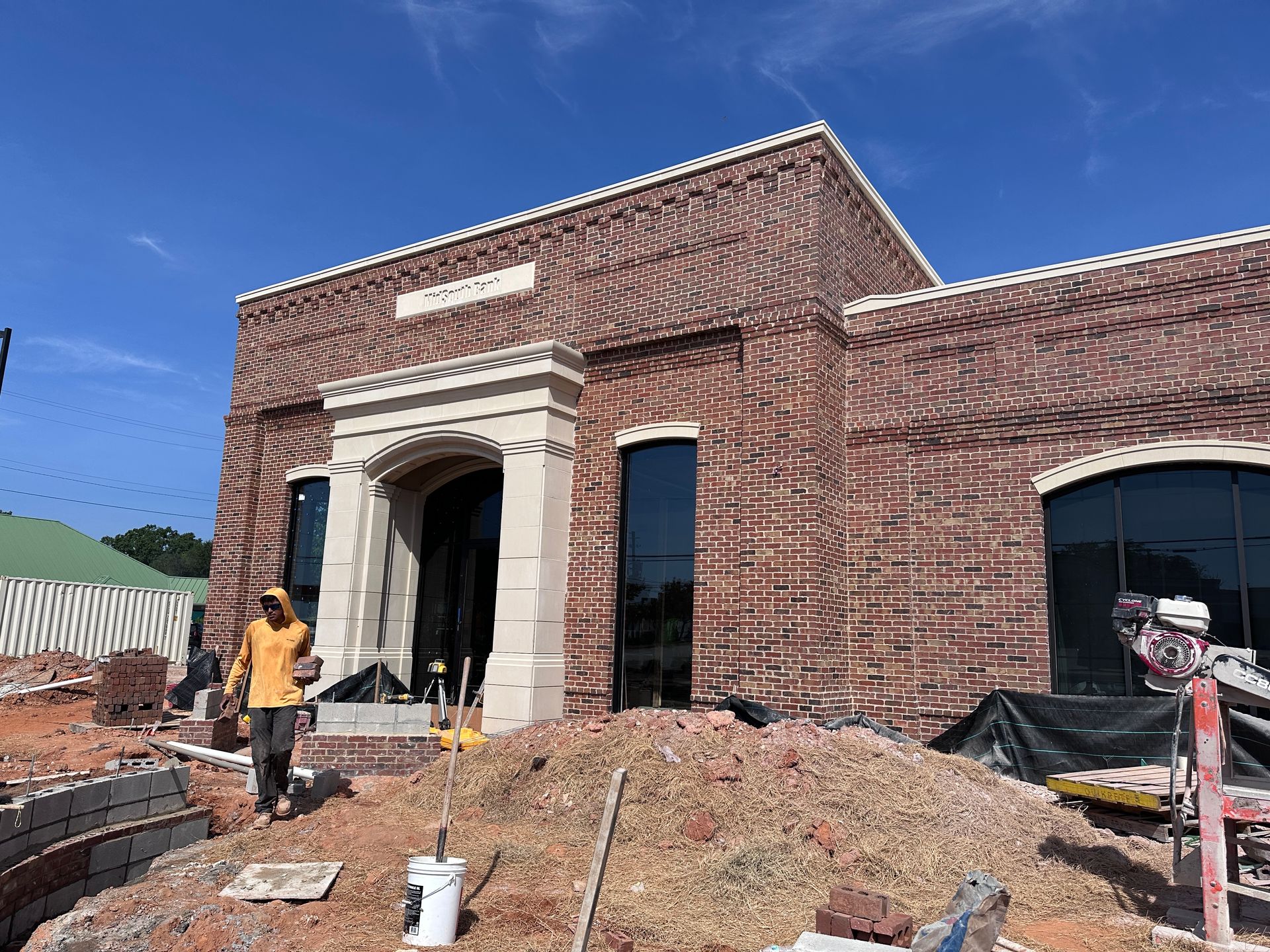 Brick building under construction with arched entrance, rubble, and a worker in a yellow shirt outdoors.