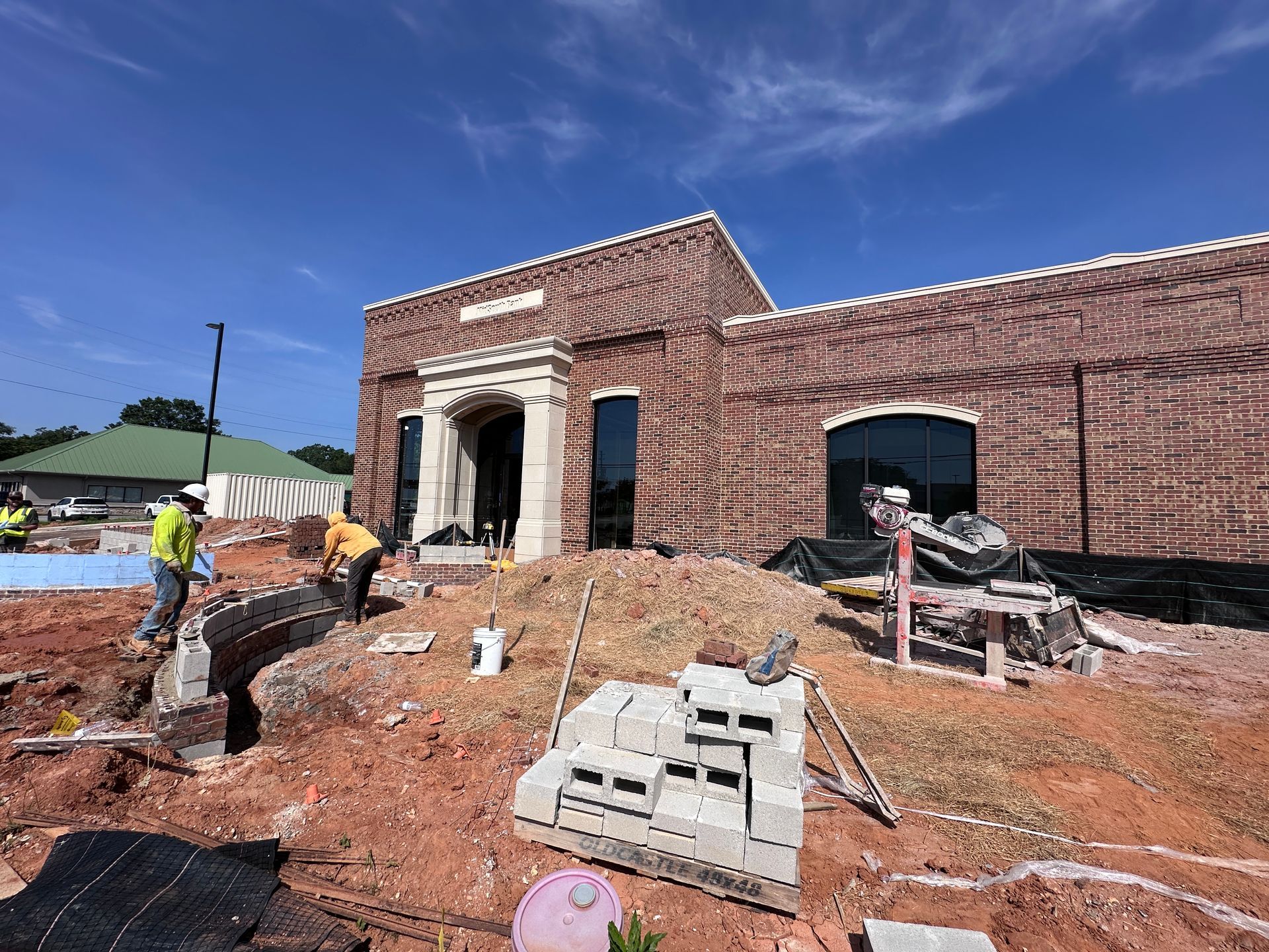 Workers at a brick building construction site with scaffolding and piles of dirt under a blue sky