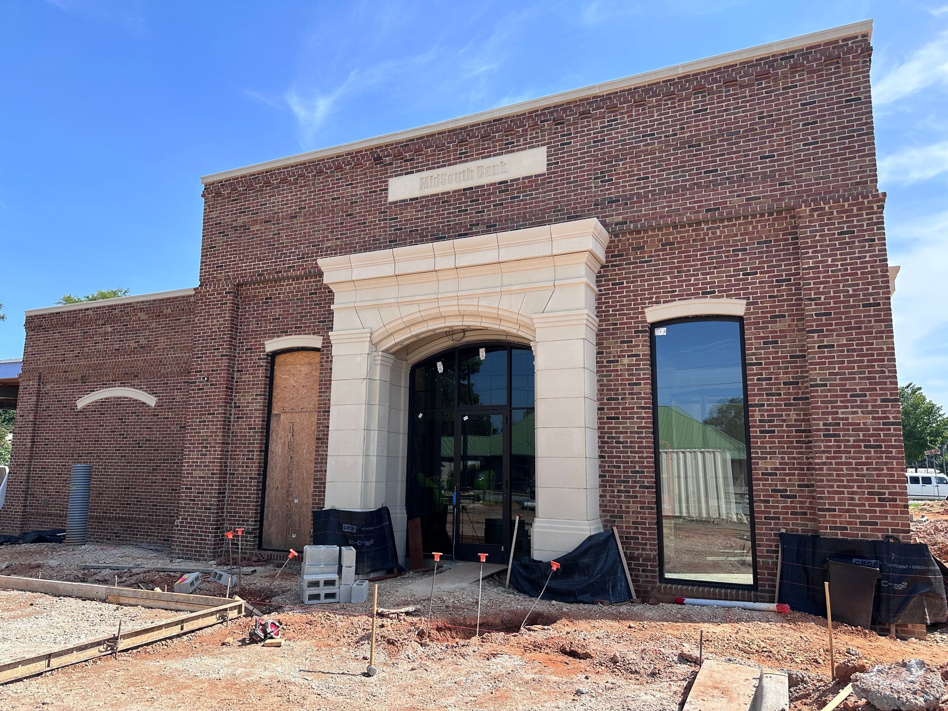Brick building entrance under construction with arched doorway, large windows, and debris in front.