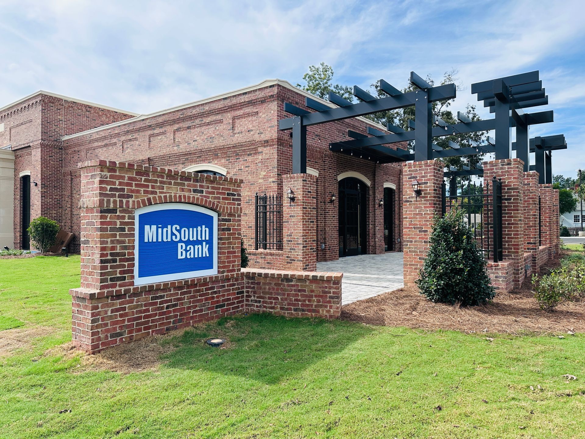 Partially built red brick bank under a blue sky, with black tarp and construction items in front.