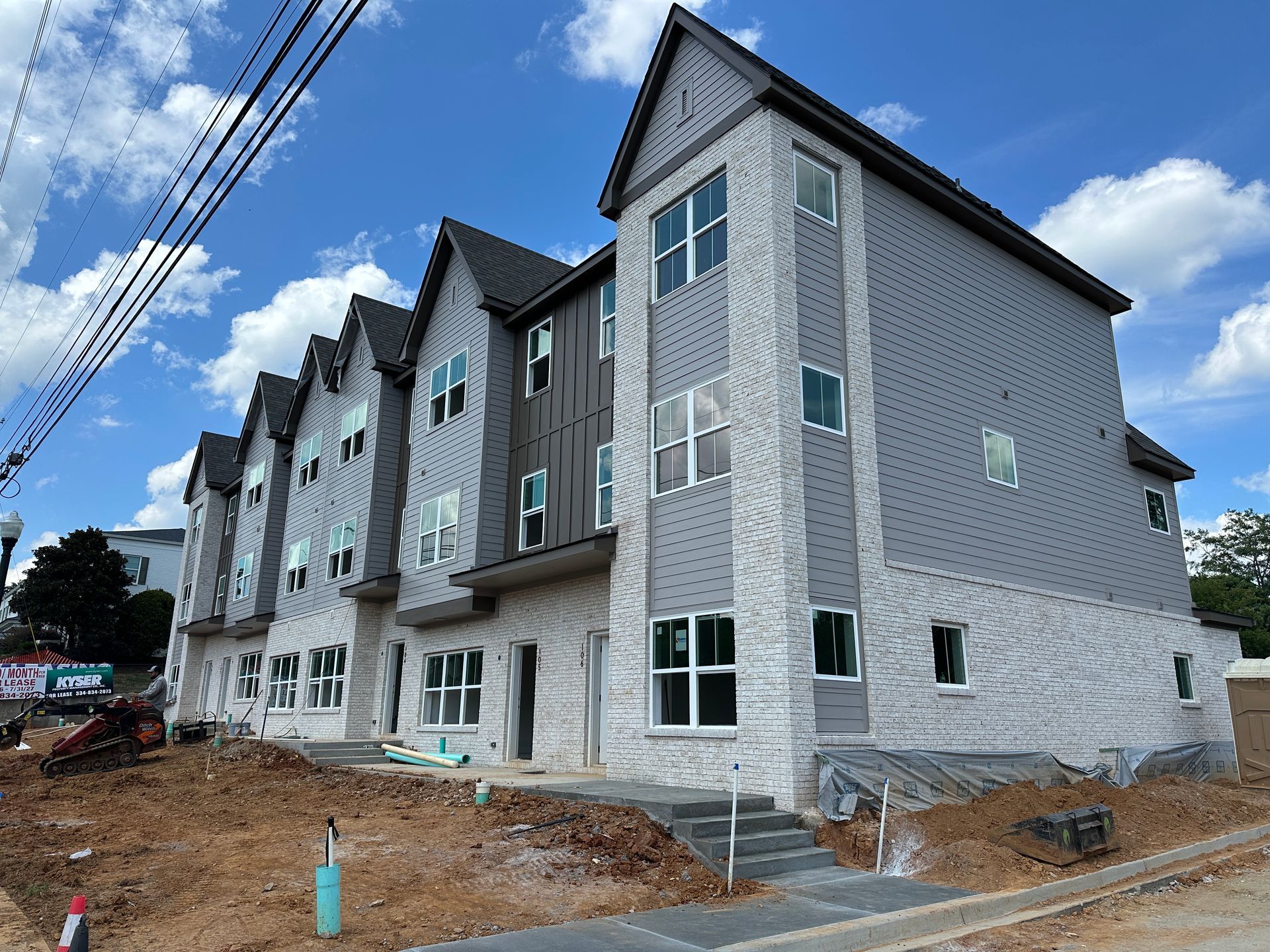 Row of new gray townhouses under construction beside a dirt lot and utility lines