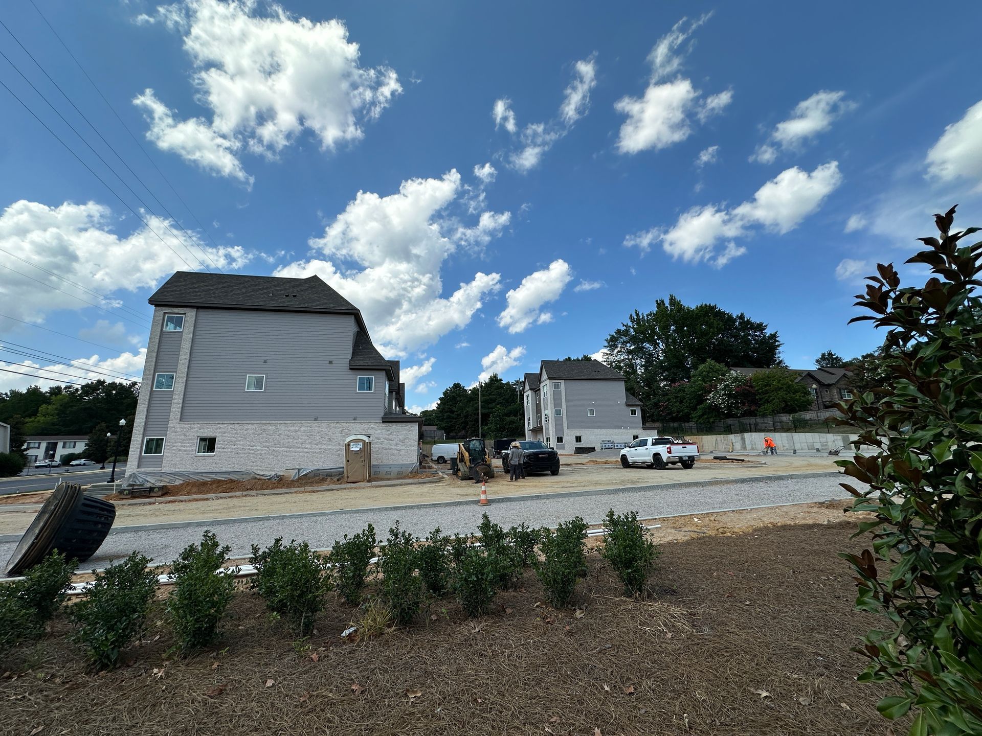 New homes under construction on a gravel lot beneath a blue sky with scattered clouds