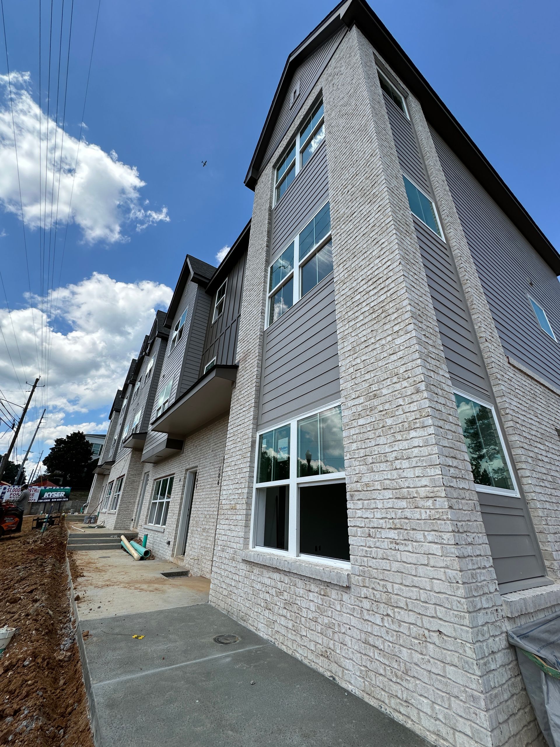 Exterior of a gray-and-white brick apartment building under a bright blue sky with clouds