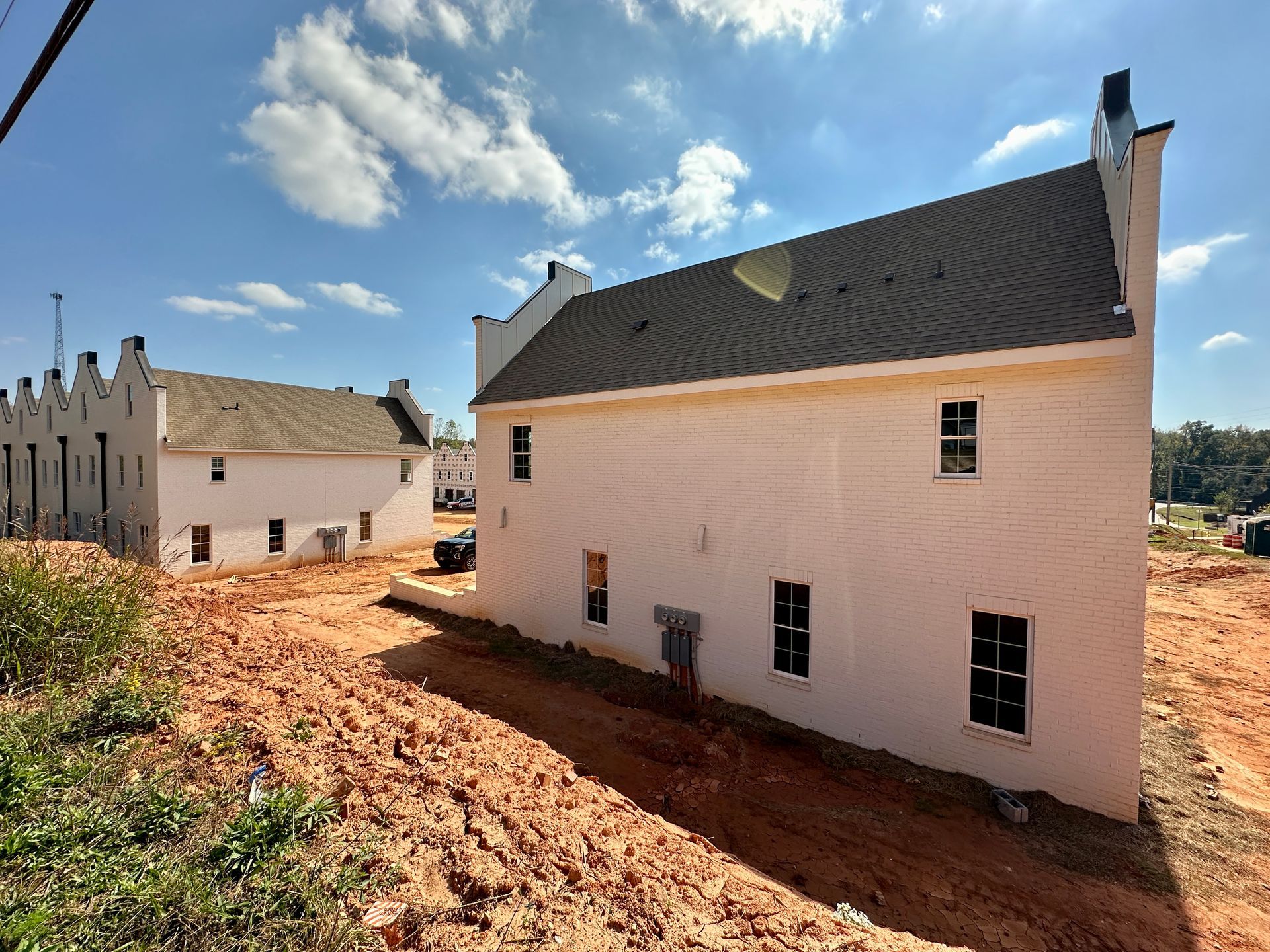 A white house with a black roof is sitting in the middle of a dirt field.
