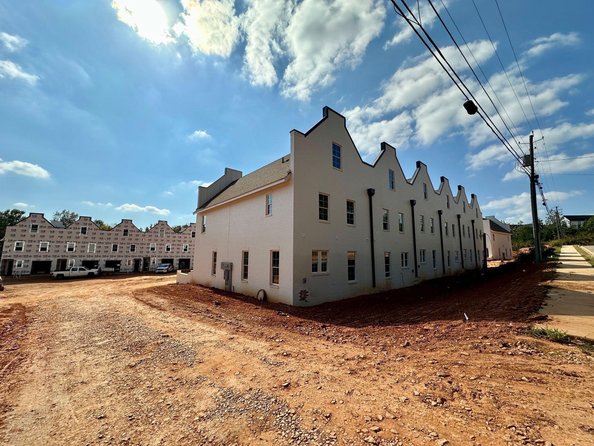 A row of white buildings are being built on a dirt road.