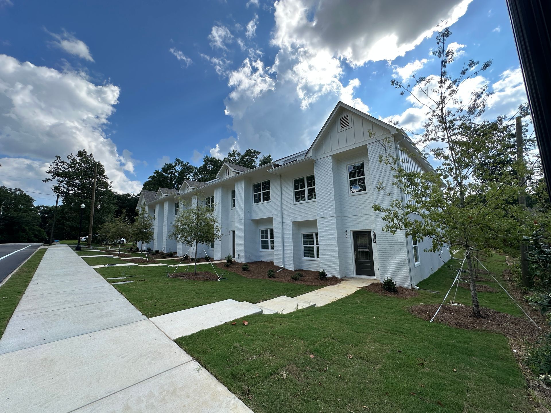 White two-story house with columns beside a sidewalk under a cloudy blue sky