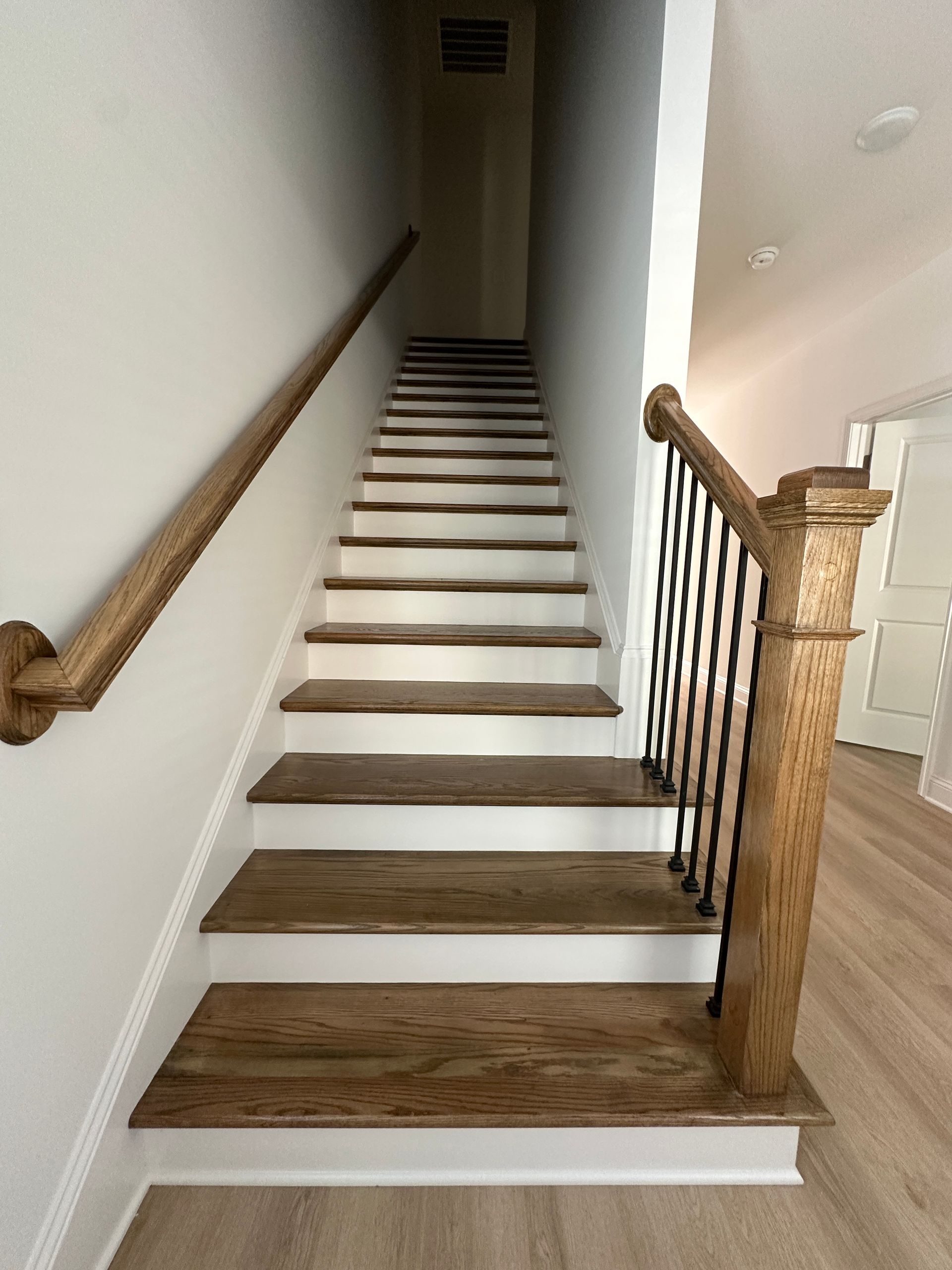 Indoor staircase with dark wood steps, white walls, and a wooden railing leading up a narrow hall