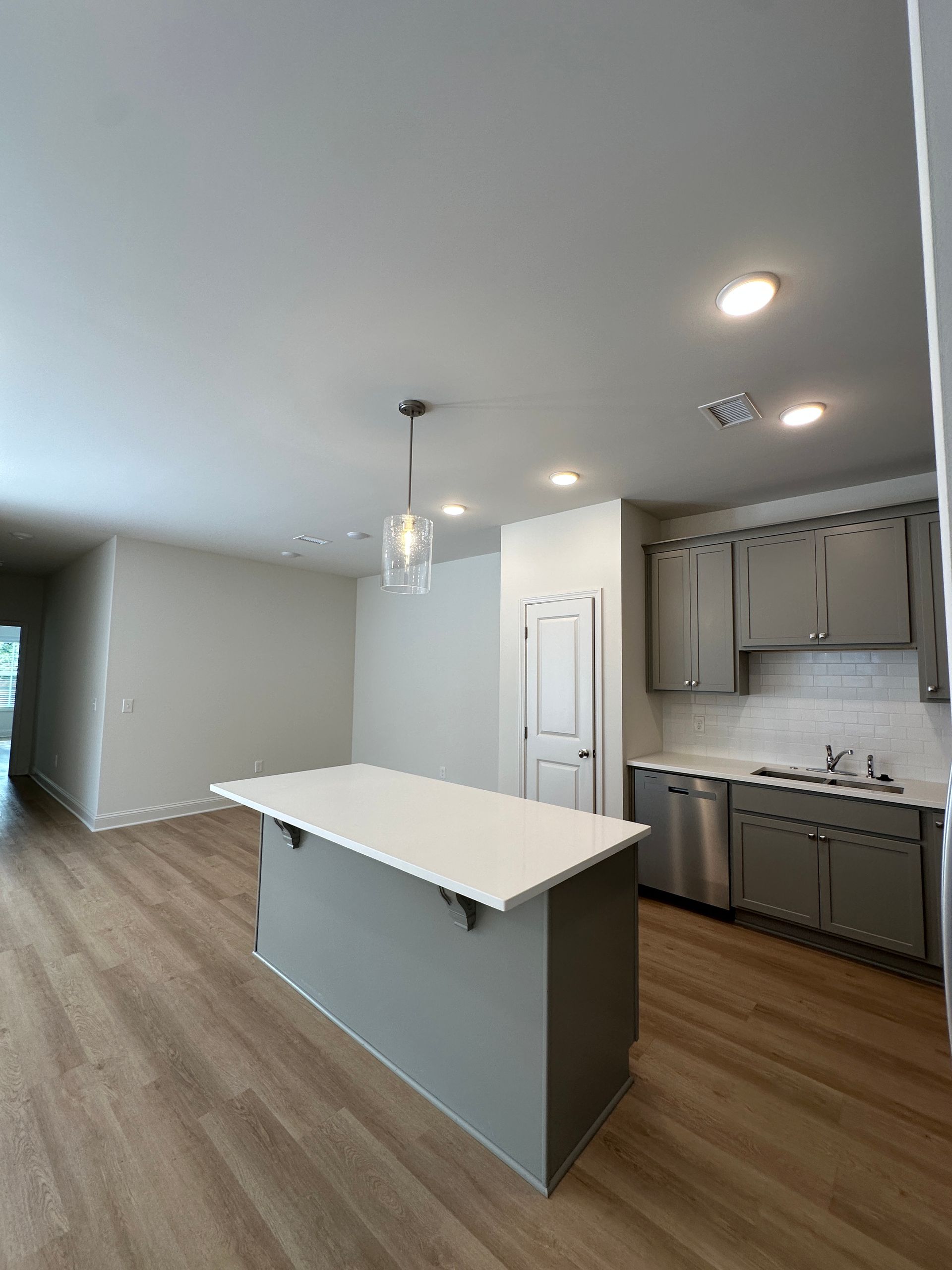 Modern kitchen with white island, gray cabinets, wood floors, and pendant lighting