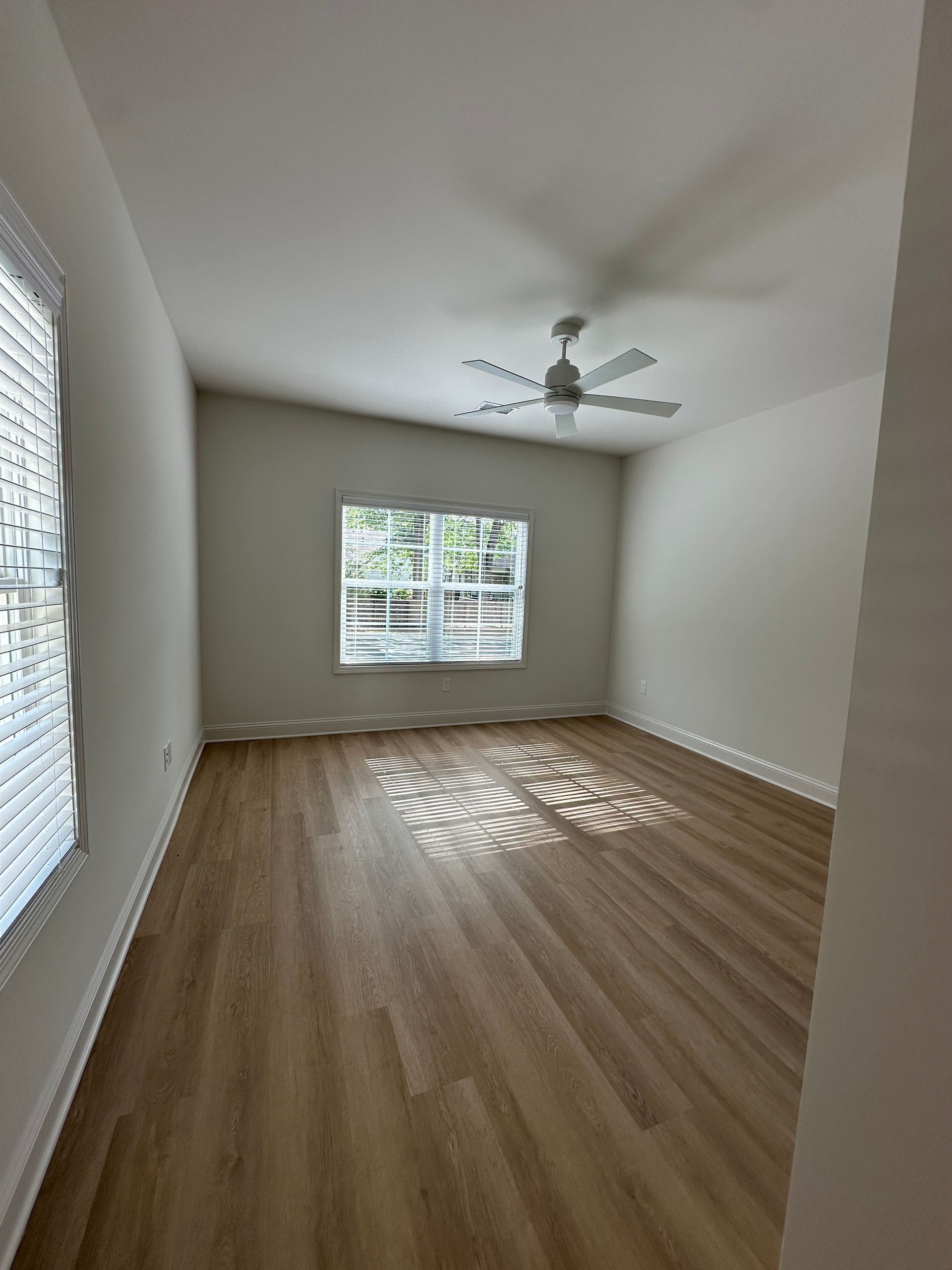 Empty white bedroom with wood flooring, window blinds, and a ceiling fan