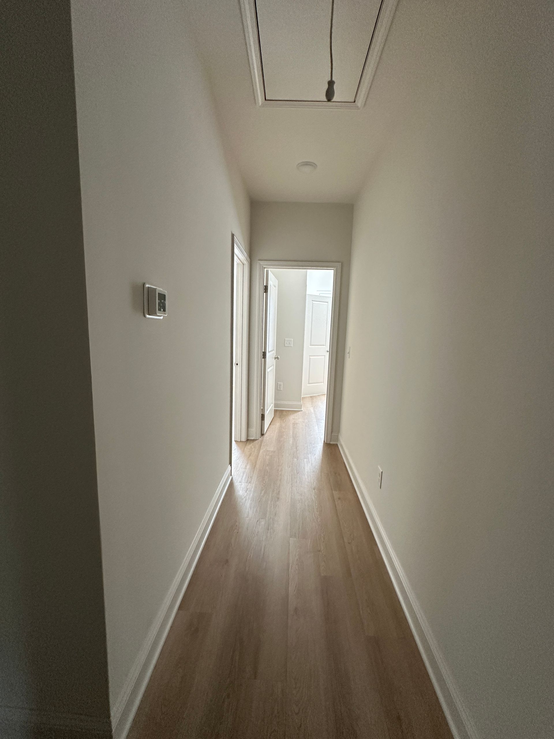 Narrow white hallway with wood floors leading to a bright doorway at the end
