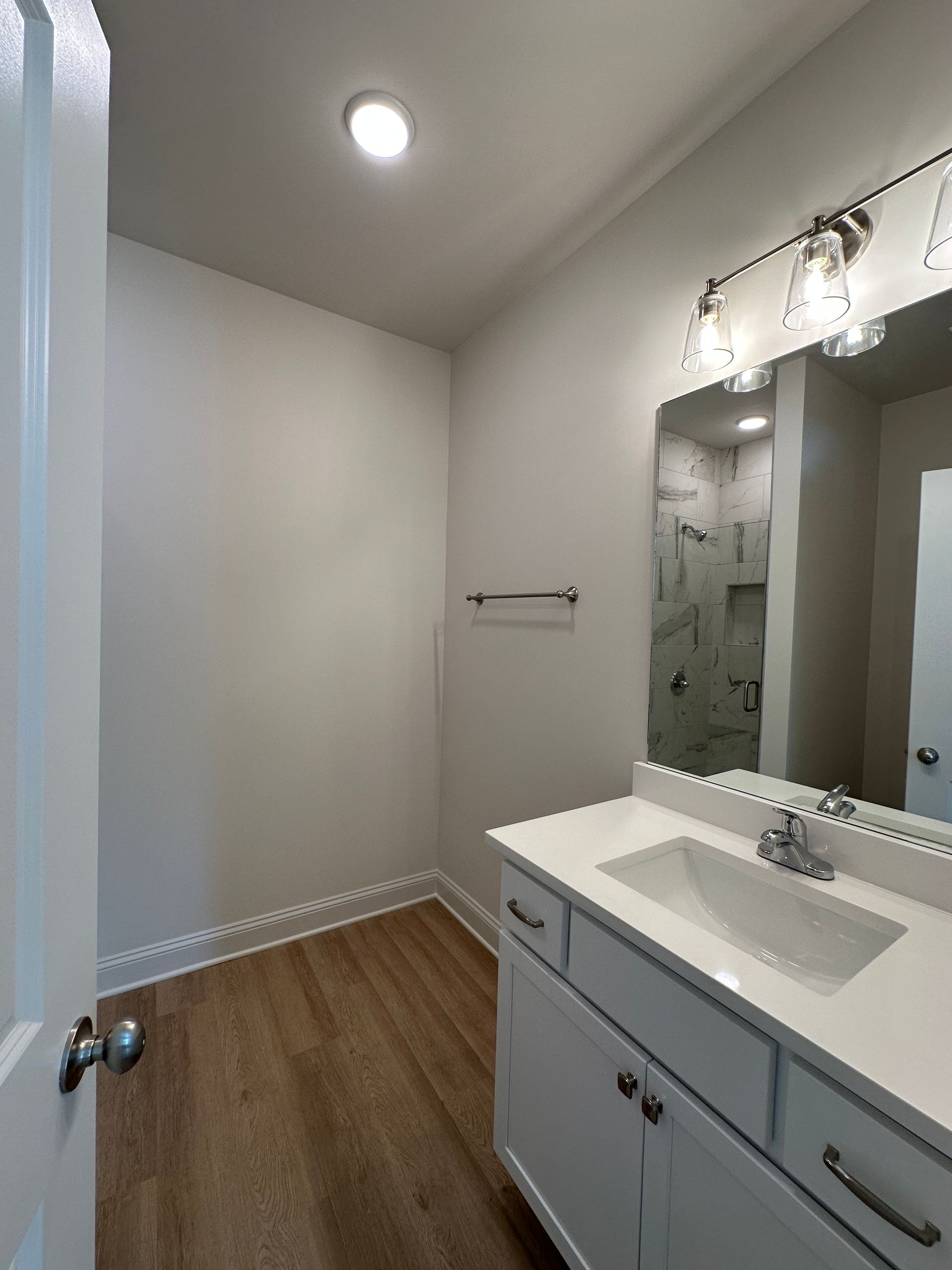 Bright bathroom with white vanity, mirror, and wood-look floor, viewed from the doorway.