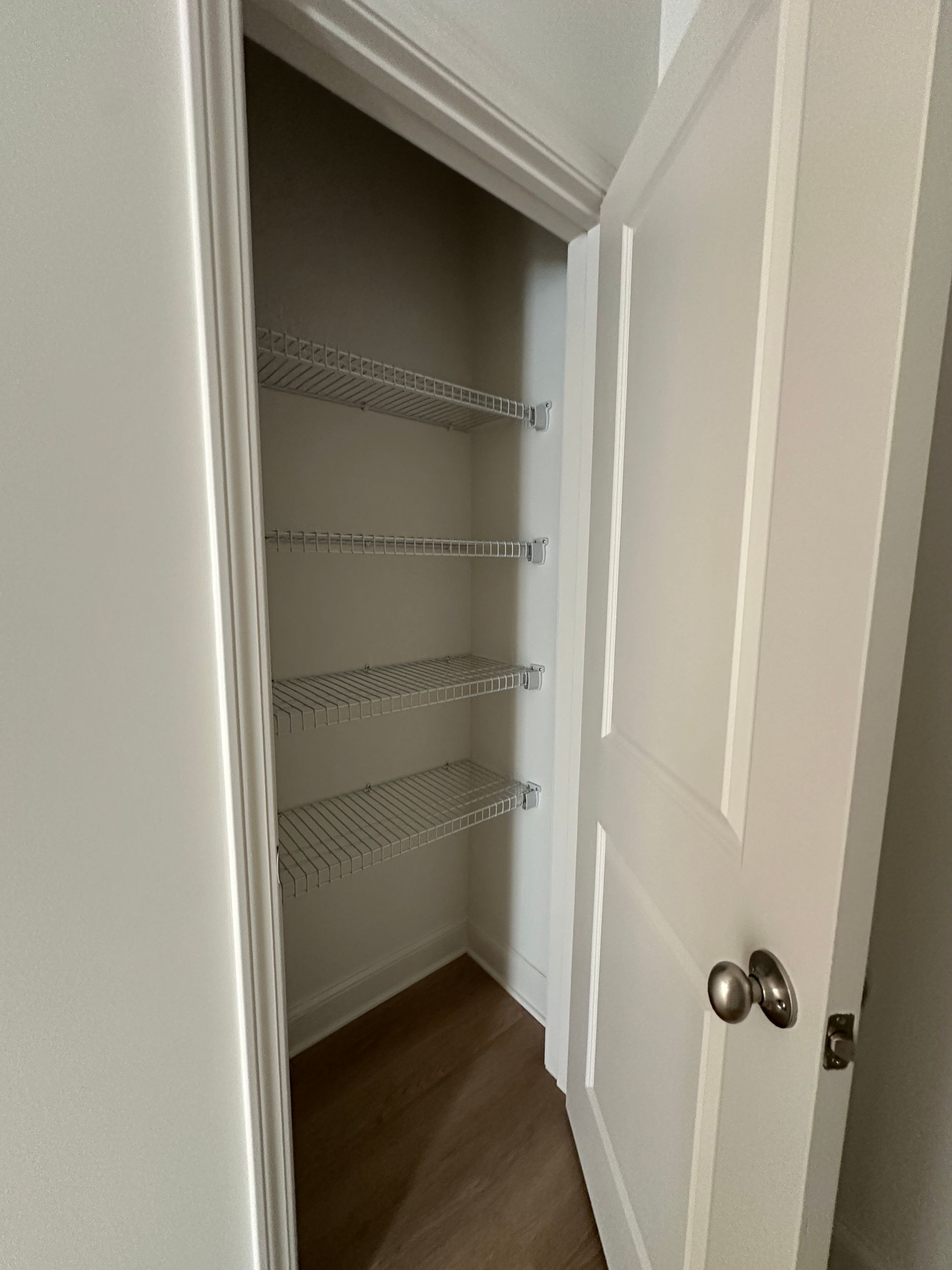 Open closet with white wire shelving and wood floor, partially blocked by a white door.