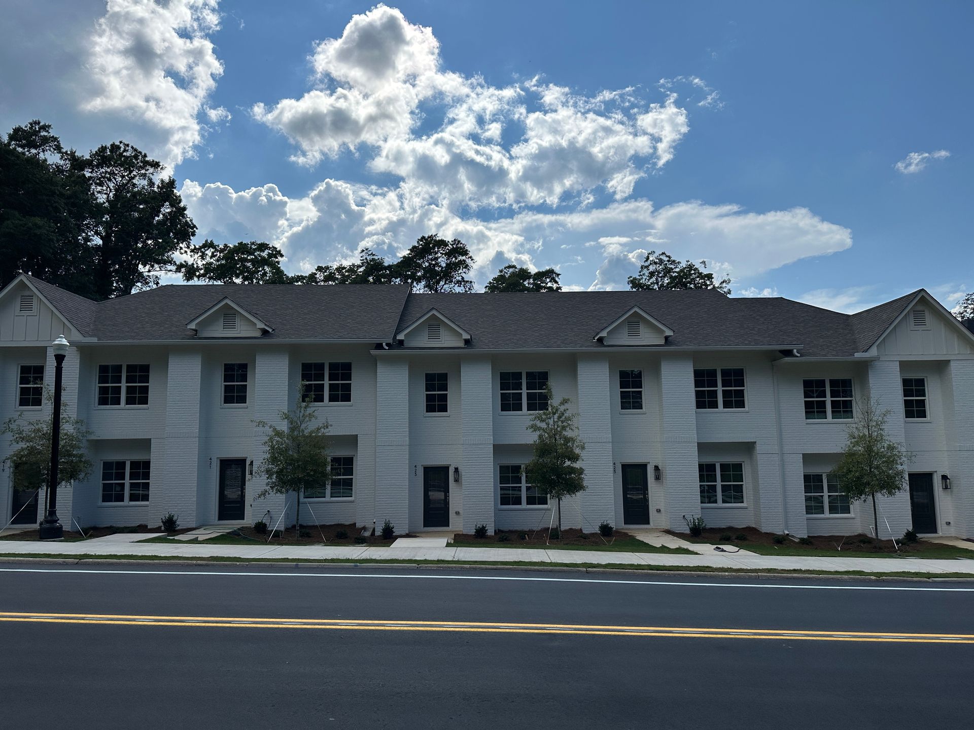 Three-story white apartment building under a cloudy blue sky beside a road