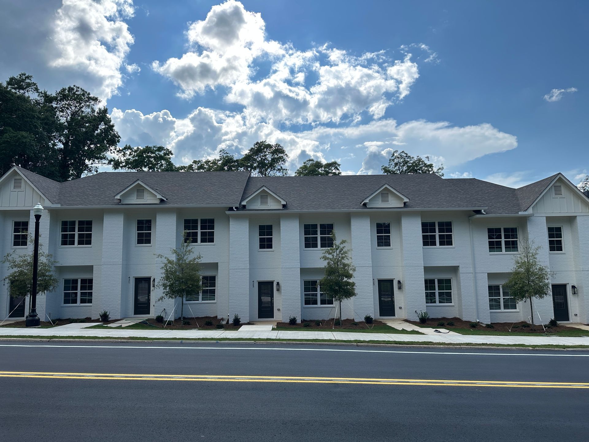 White two-story apartment building with gray roof under a blue sky with clouds