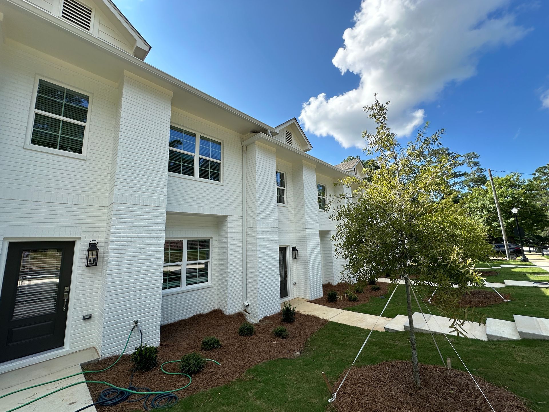 White apartment building with black doors, green lawn, and a small tree under a blue sky