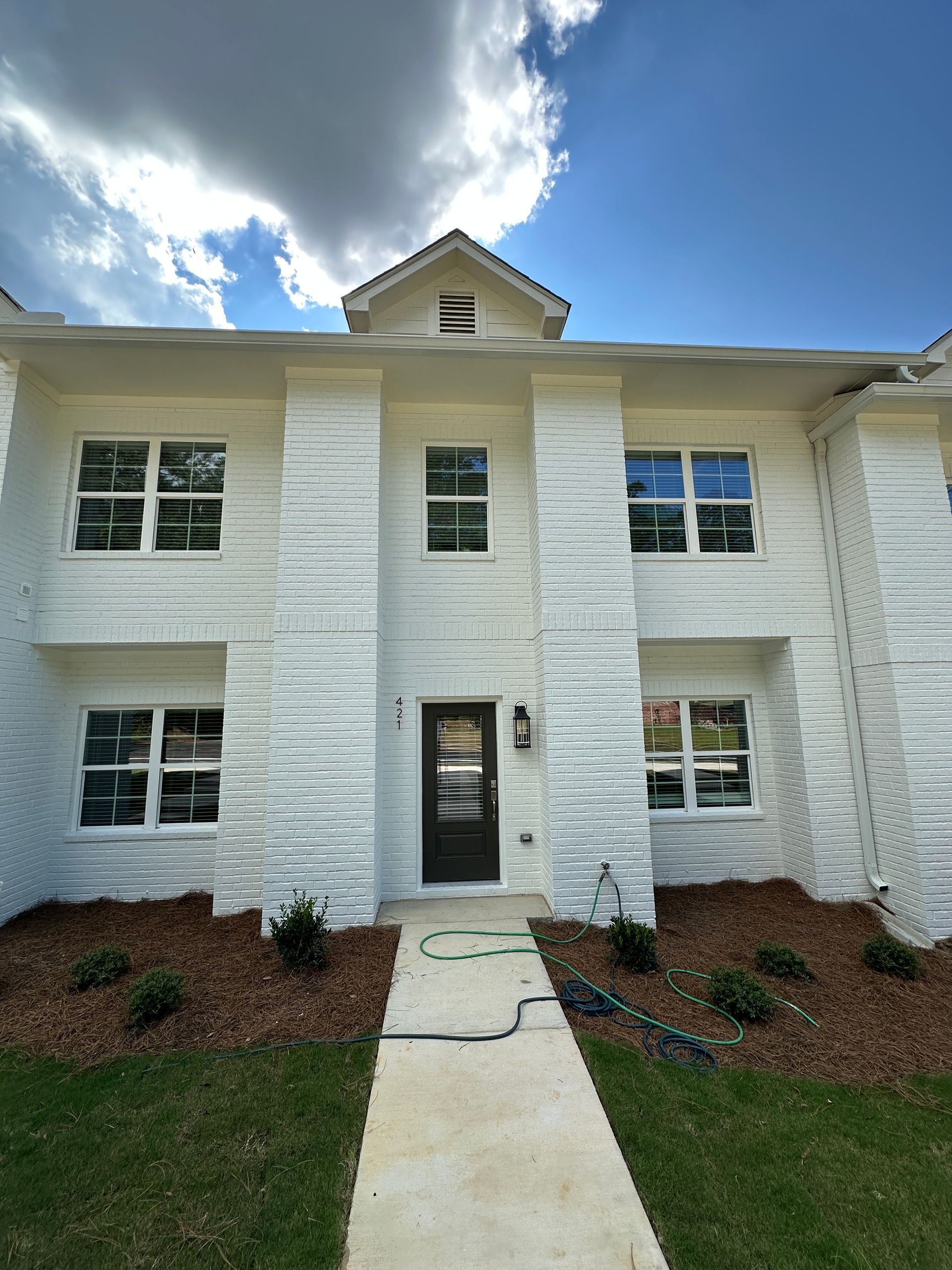 Front view of a white two-story townhouse with a central walkway and small front lawn