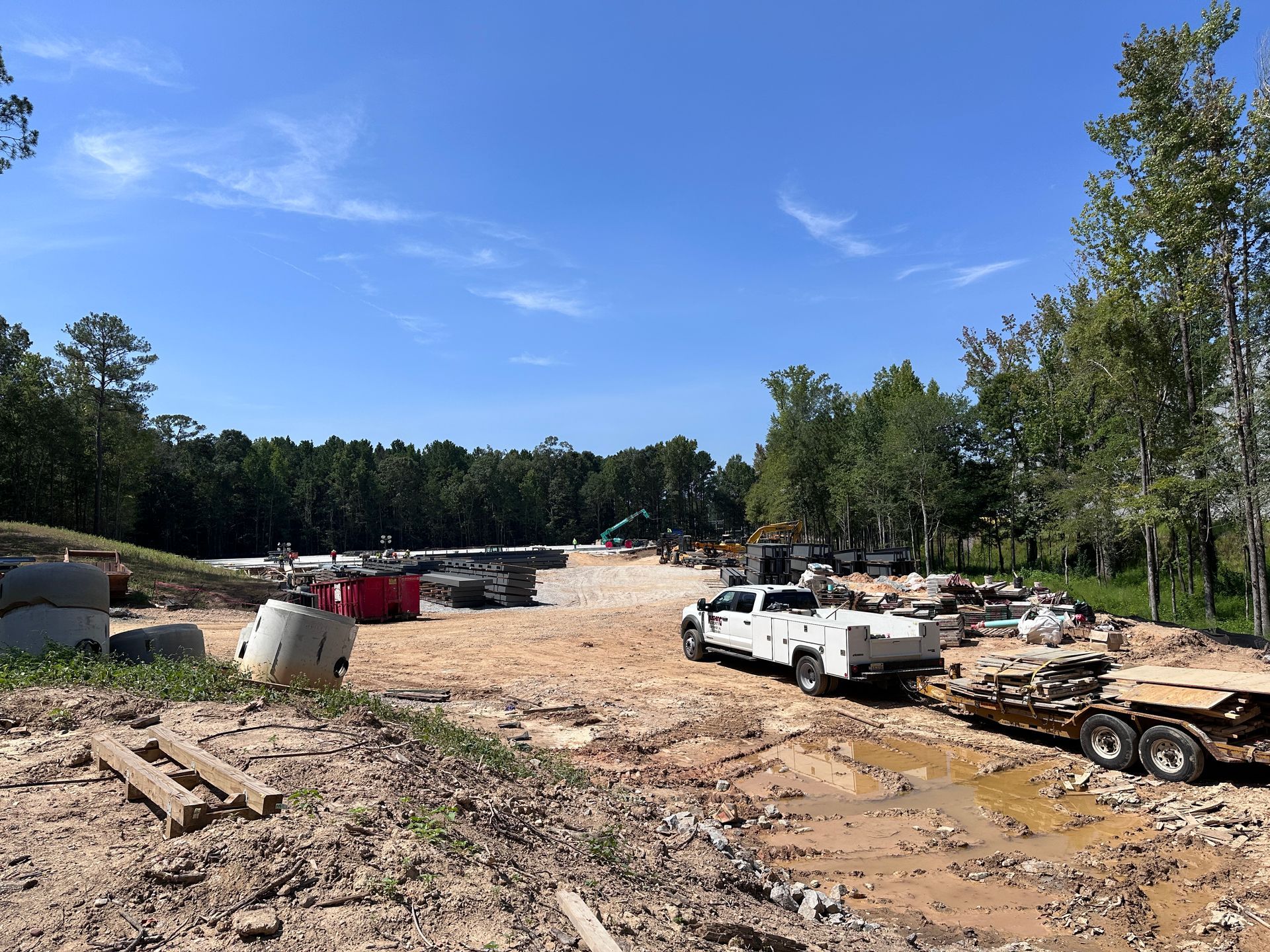 Construction site with dirt roads, white trucks, and trees under a clear blue sky