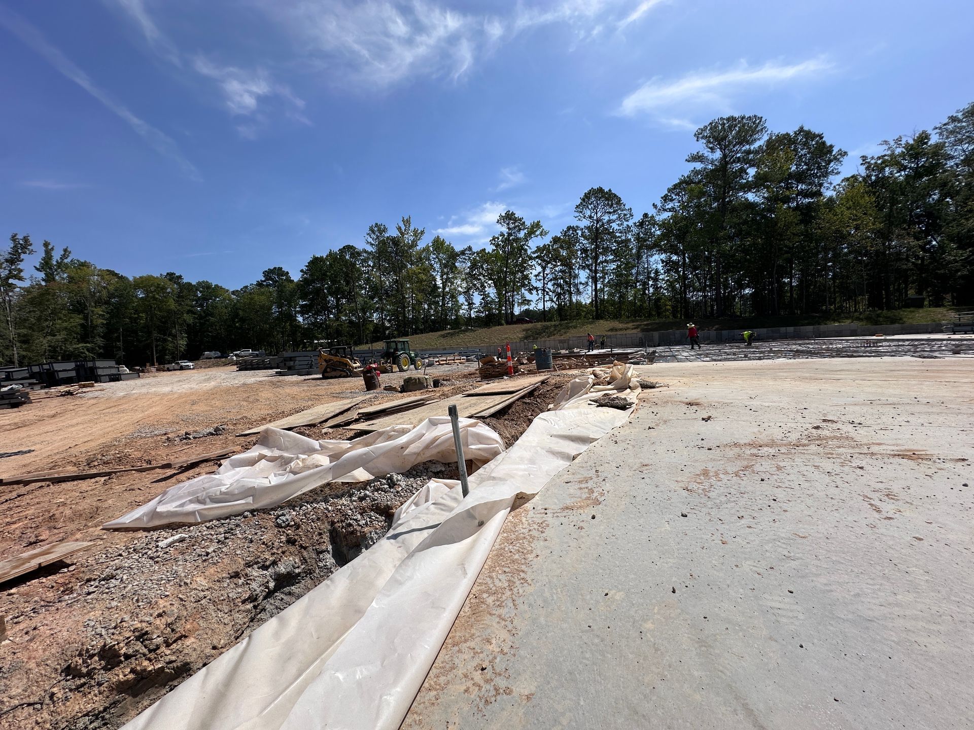 Flooded construction site with muddy ground, silt barriers, and trees under a blue sky