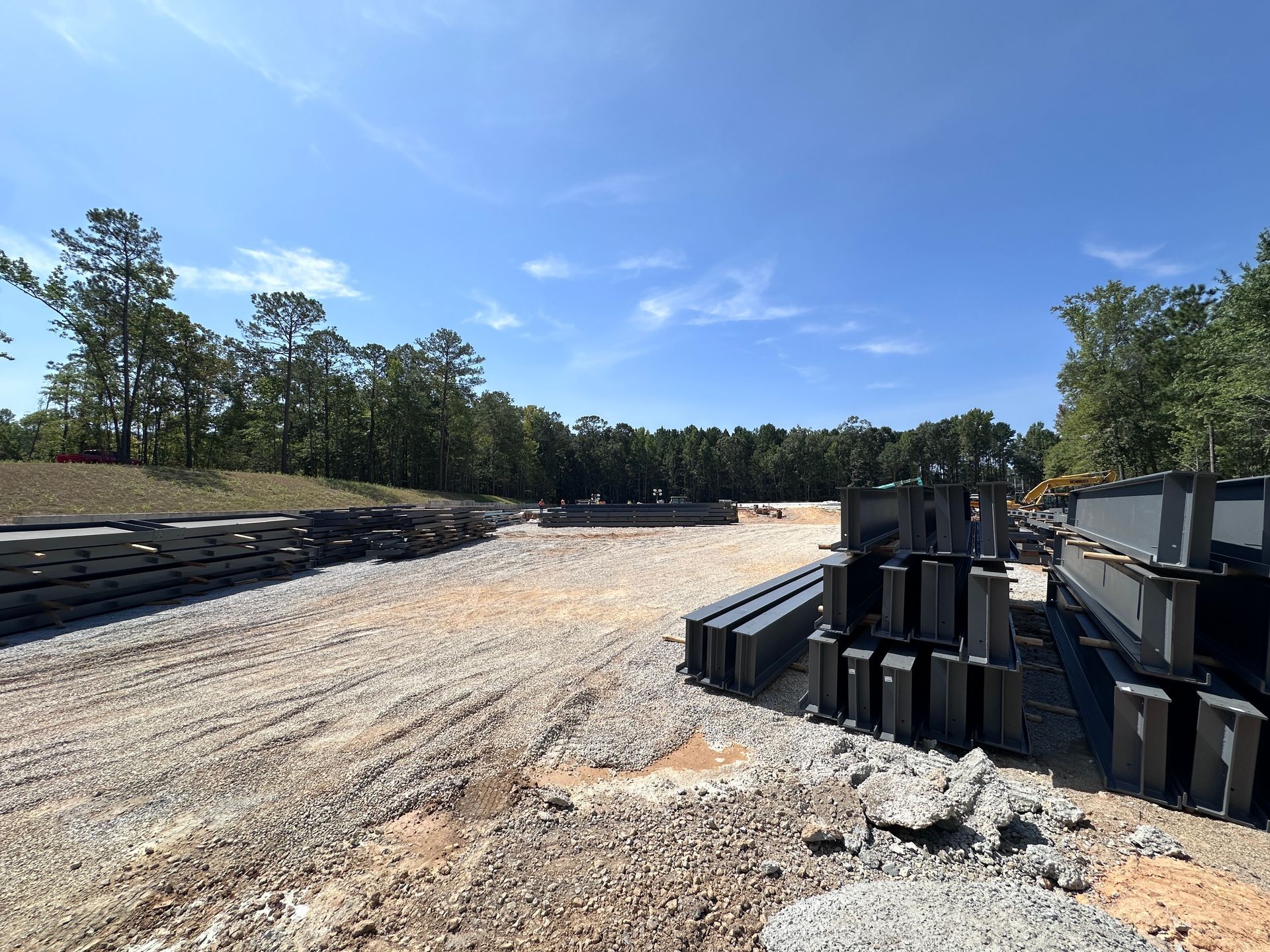 Construction site with gravel, stacked materials, and trees under a clear blue sky