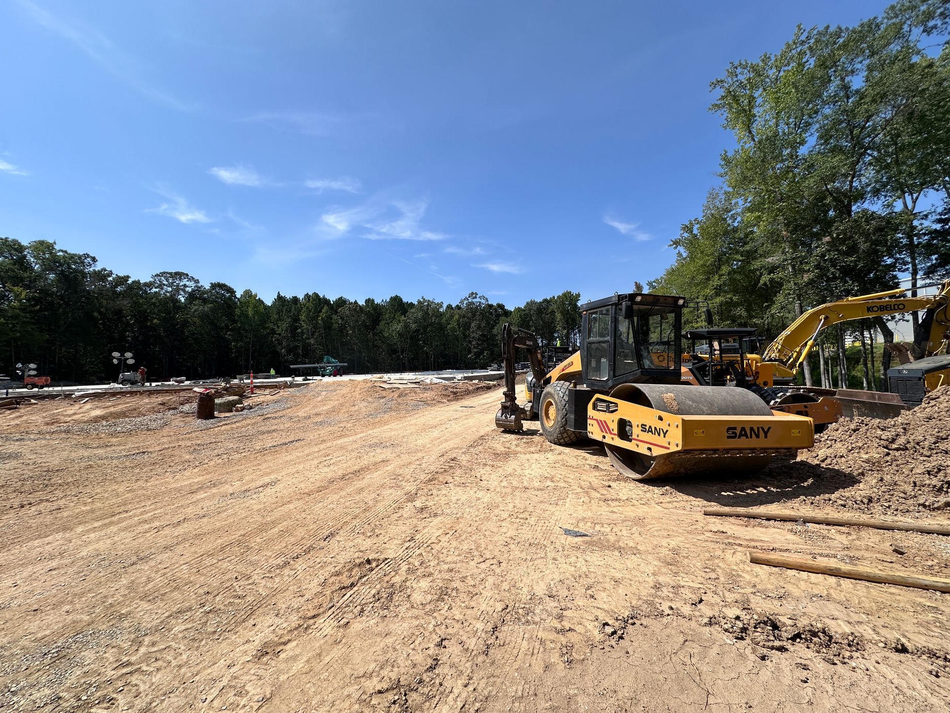Construction site with excavators and a bulldozer on a dirt lot under a blue sky