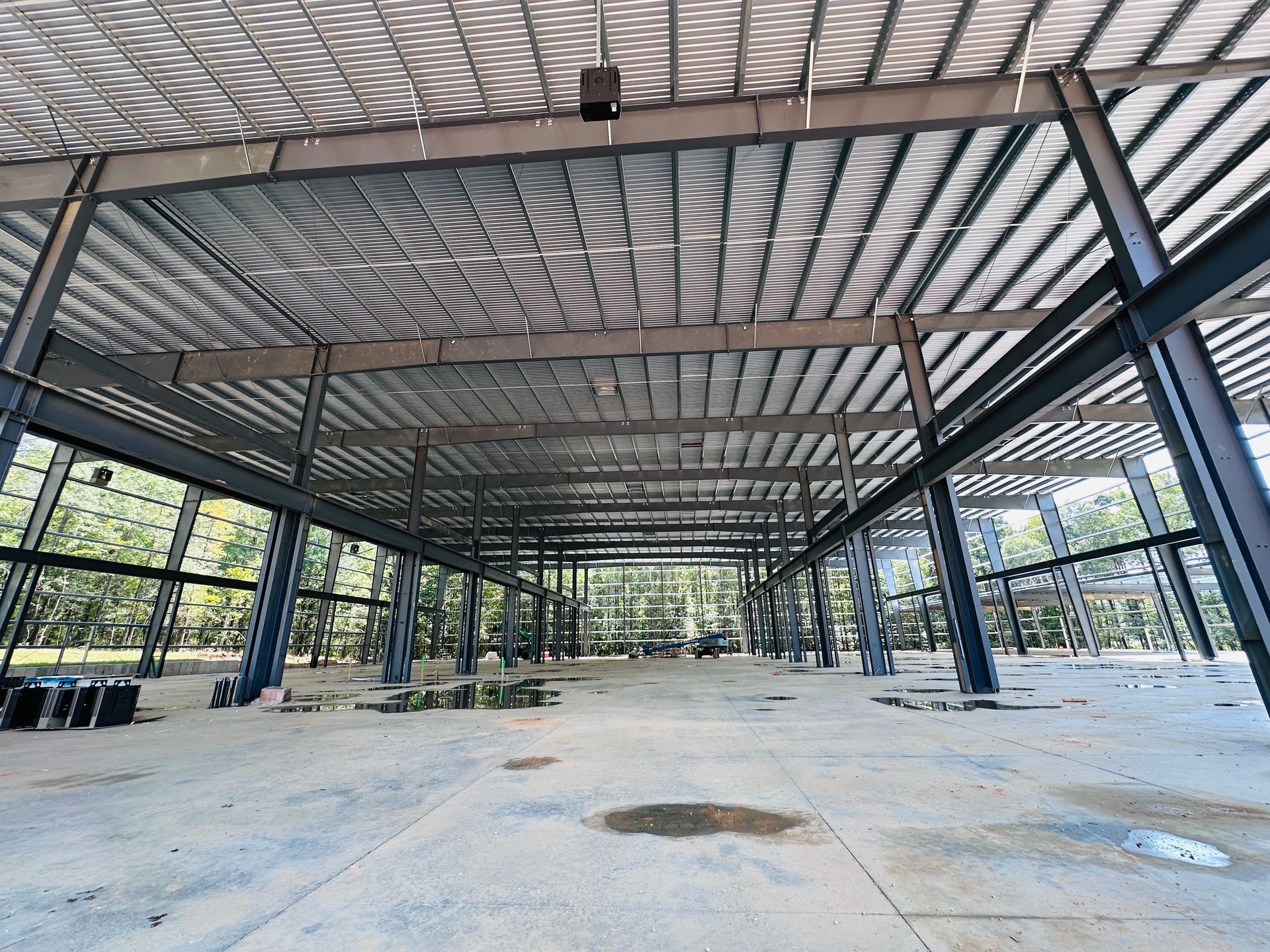 Empty open-sided pavilion with steel beams and a patterned metal roof over a concrete floor