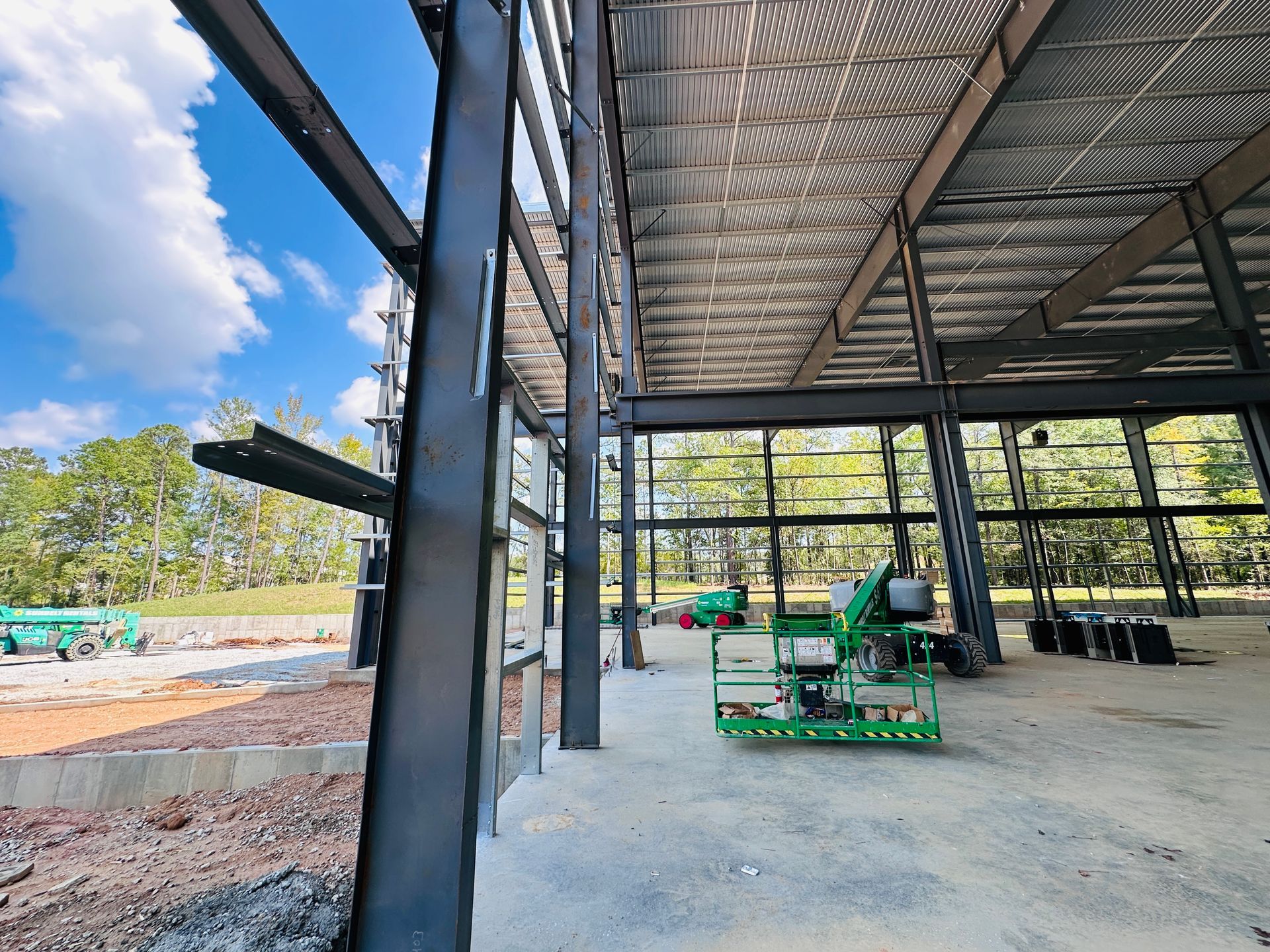 Steel-frame building under construction with concrete floor, scaffolding, and blue sky visible outside