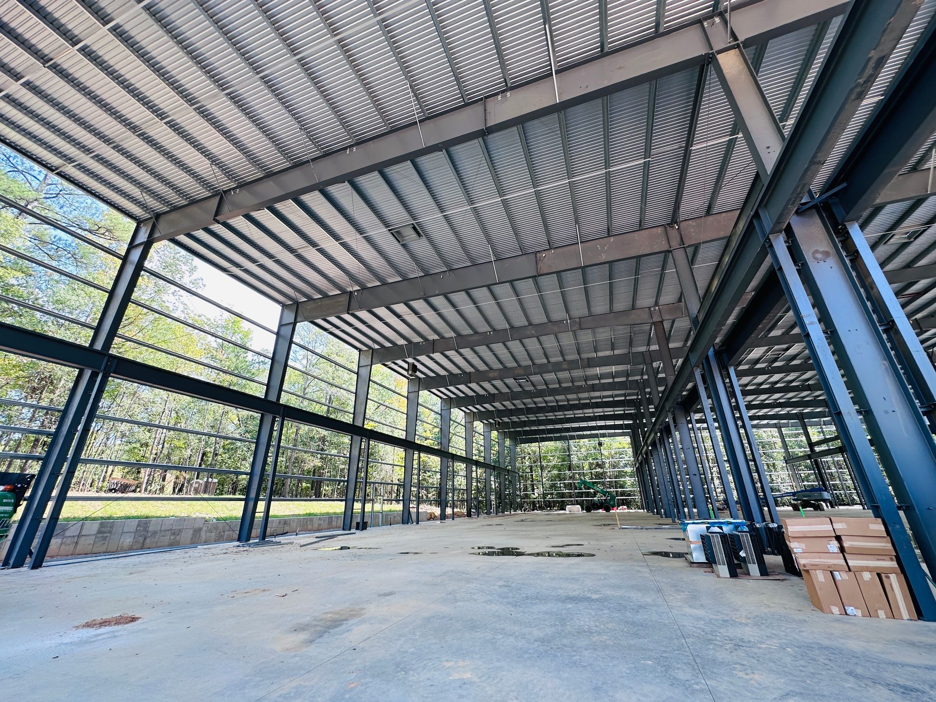 Empty steel warehouse interior with corrugated roof, concrete floor, and stacked boxes along the right side