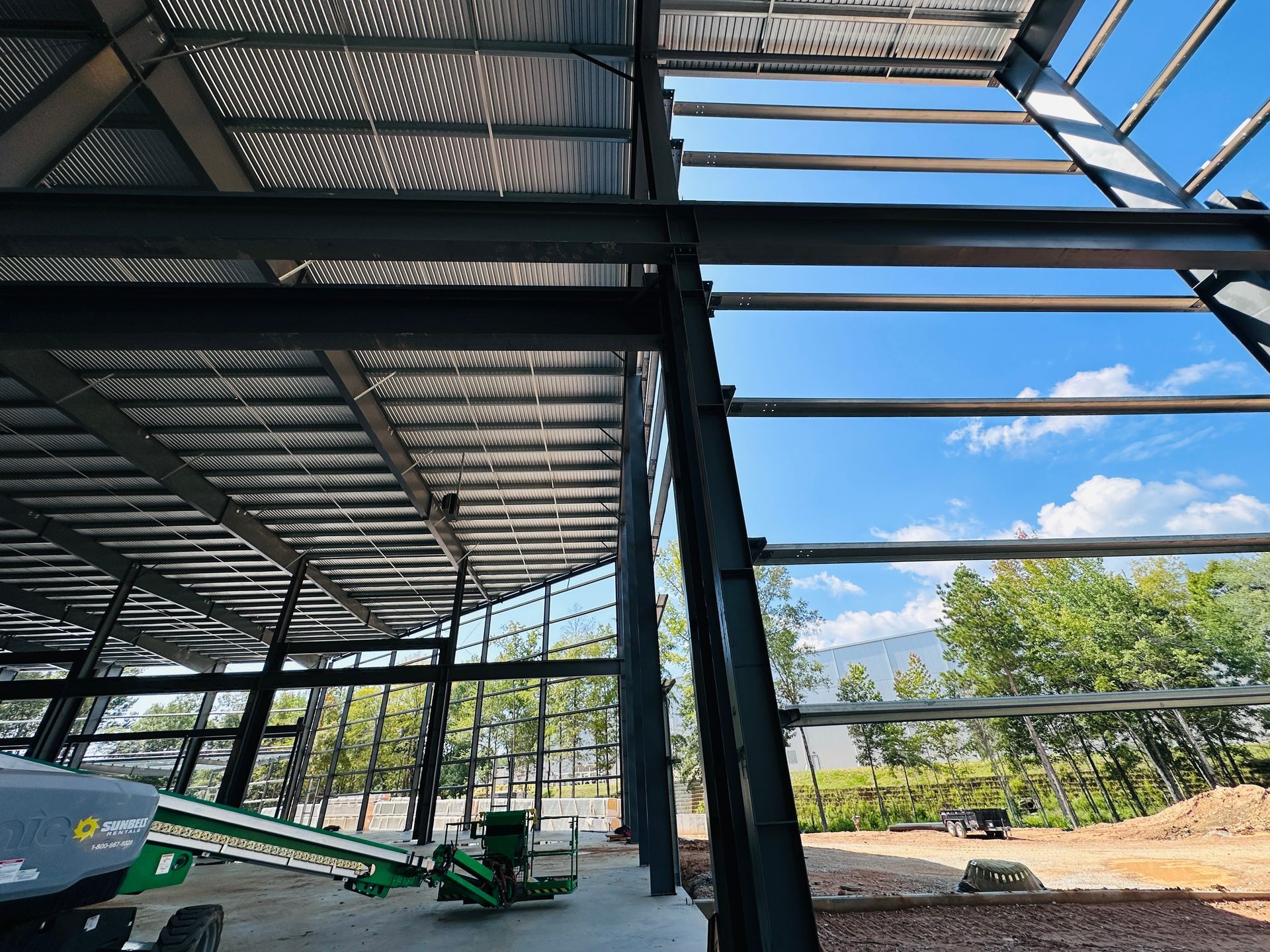 Steel-framed building under construction with corrugated roof panels and a clear blue sky in the background