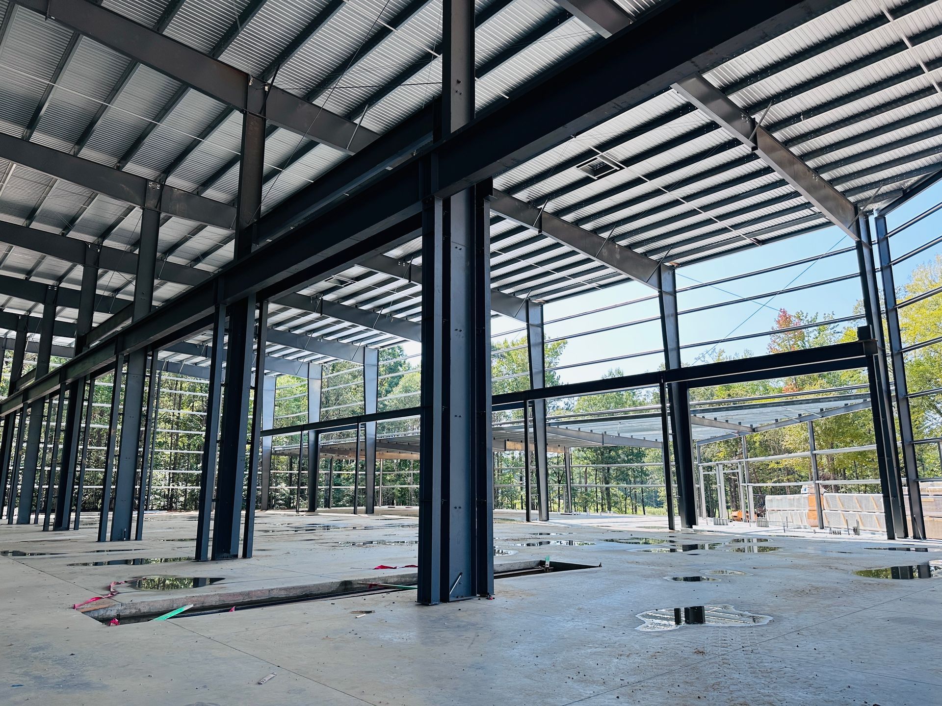 Empty steel-frame building interior with a corrugated roof and concrete floor under construction