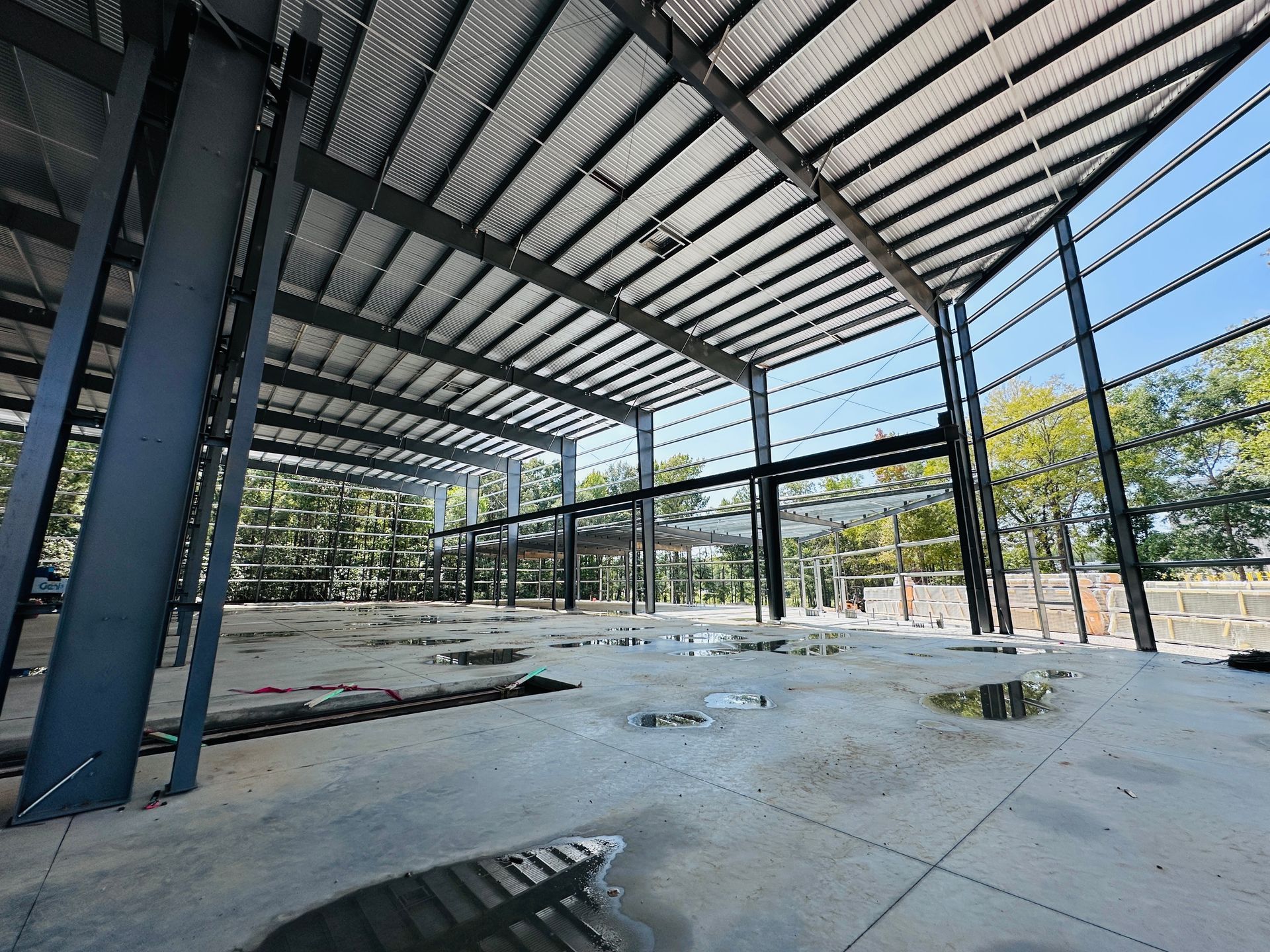 Empty steel-framed building interior with concrete floor, large windows, and exposed roof beams