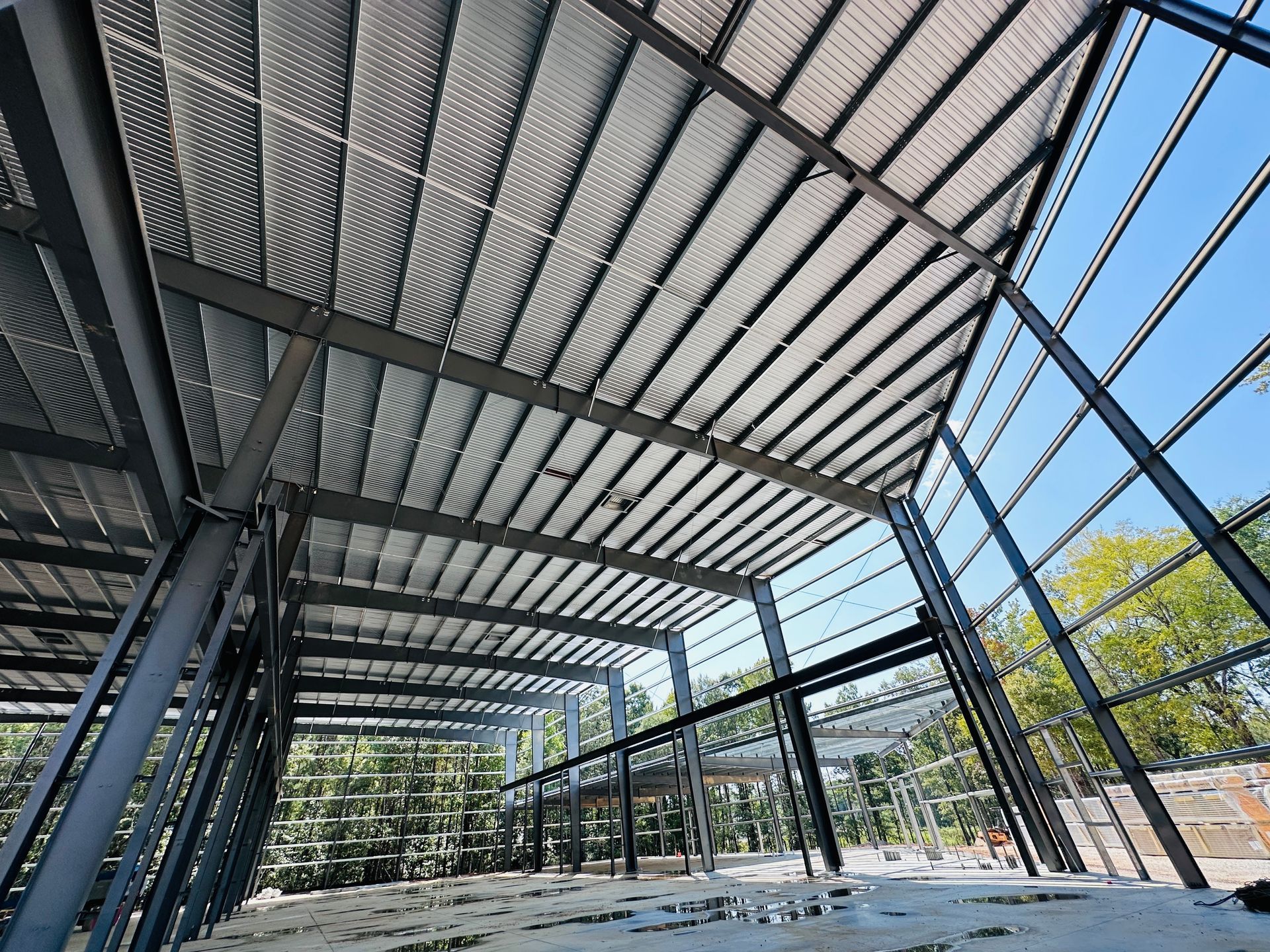 Steel-framed pavilion with slanted metal roof and open sides, overlooking trees and a blue sky